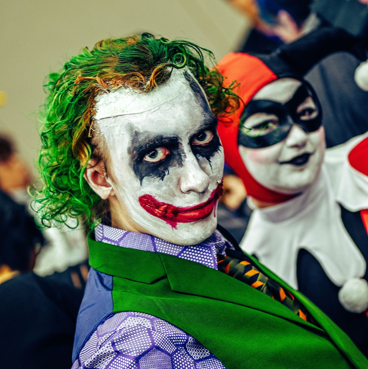 Cosplayers dressed as Joker and Harley Quinn characters at comic convention.