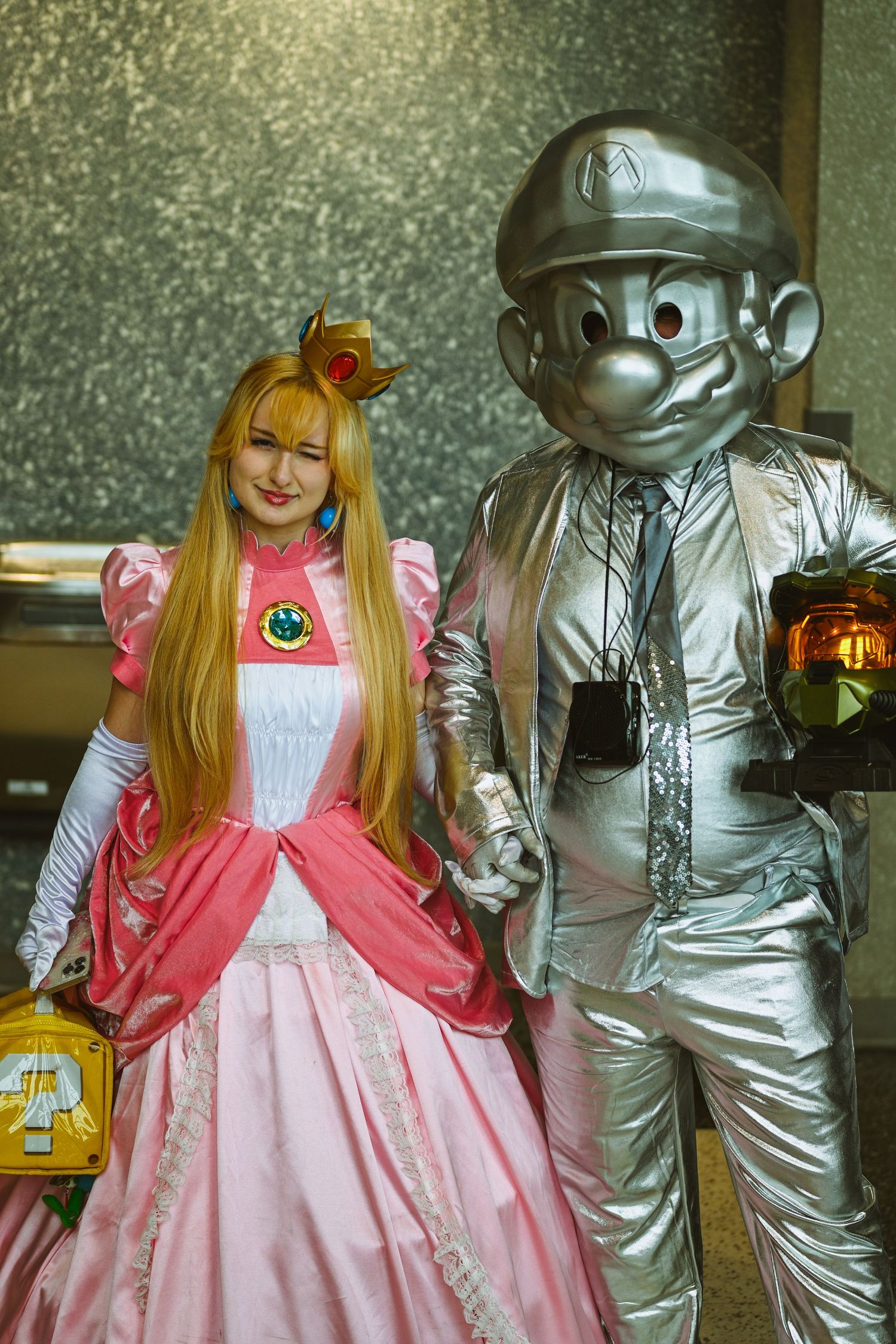 Cosplay scene with figure in pink dress posing next to character in metallic silver costume.