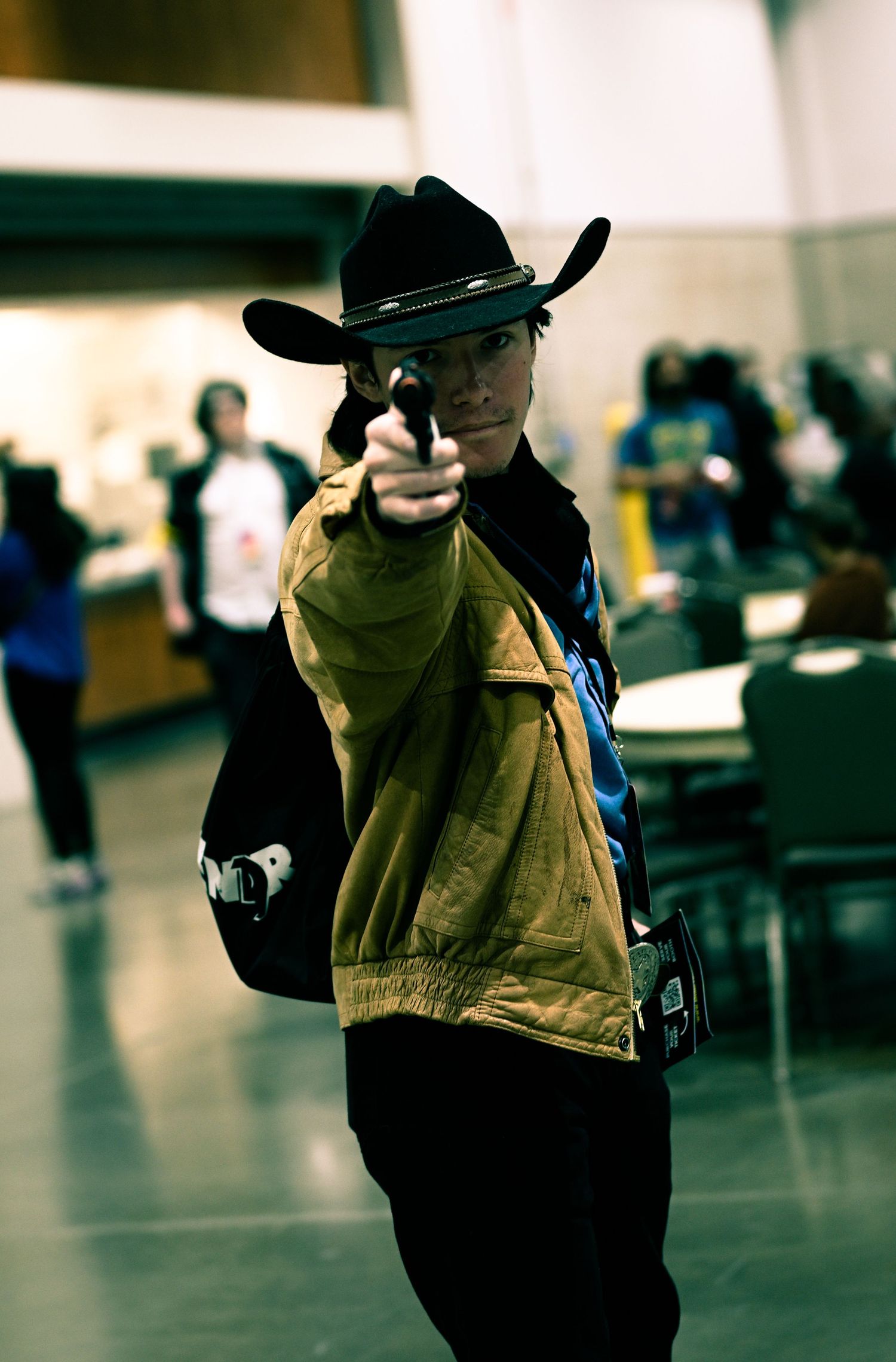 Person in cowboy hat and vest poses dramatically in convention center.