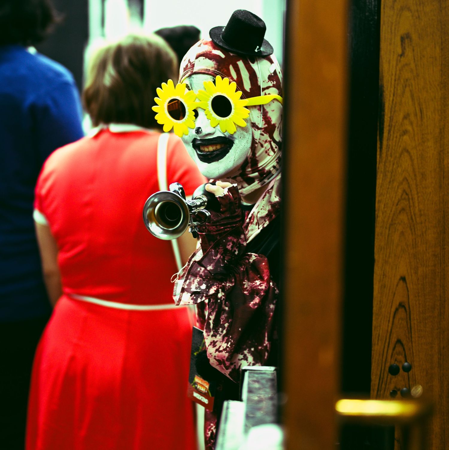 Cosplayer wearing sunflower mask and holding camera at convention.