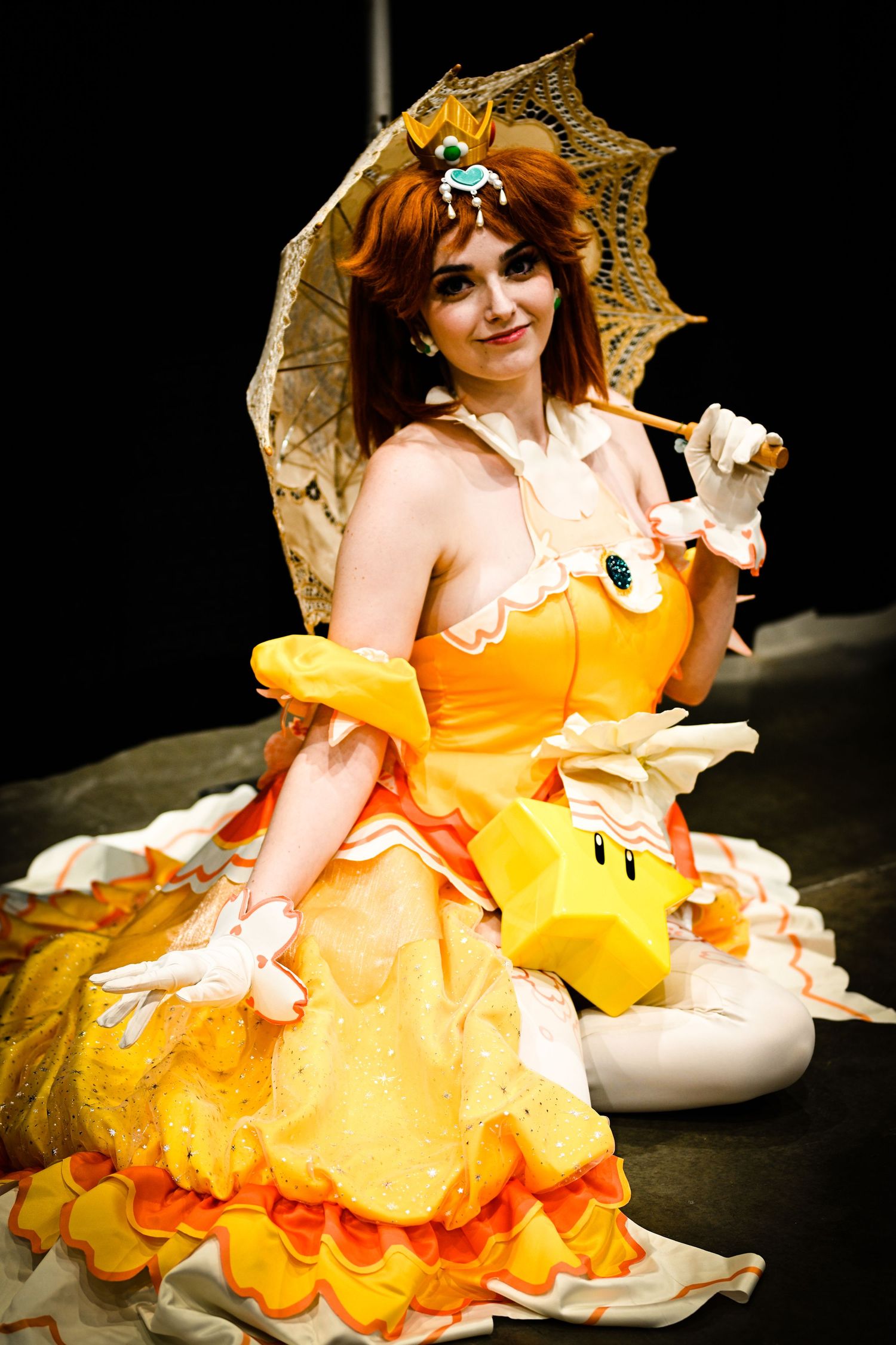 Person in vibrant orange Victorian-style dress with parasol performing on stage.