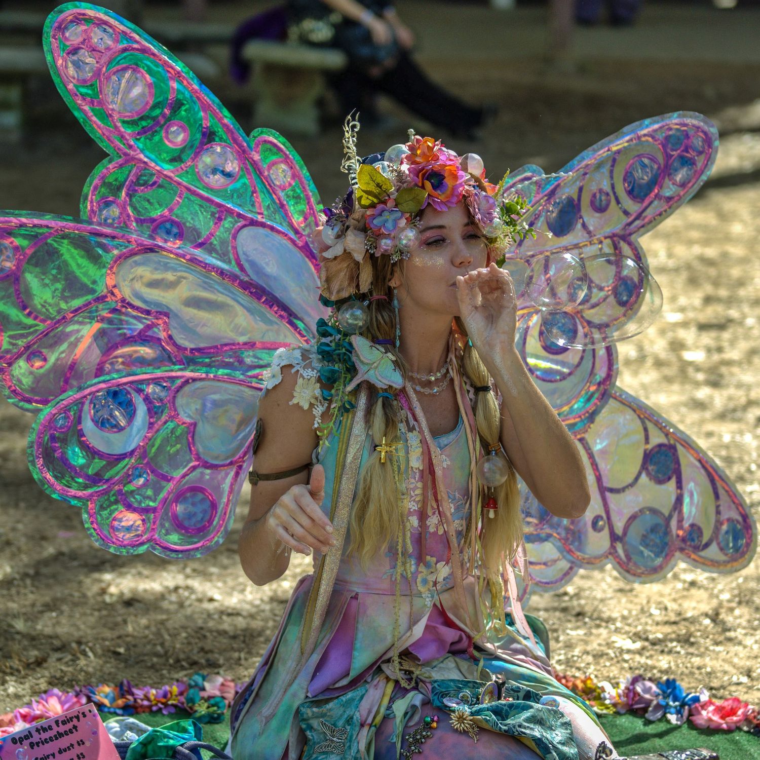 Fairy performer in iridescent wings and floral crown at a renaissance festival.