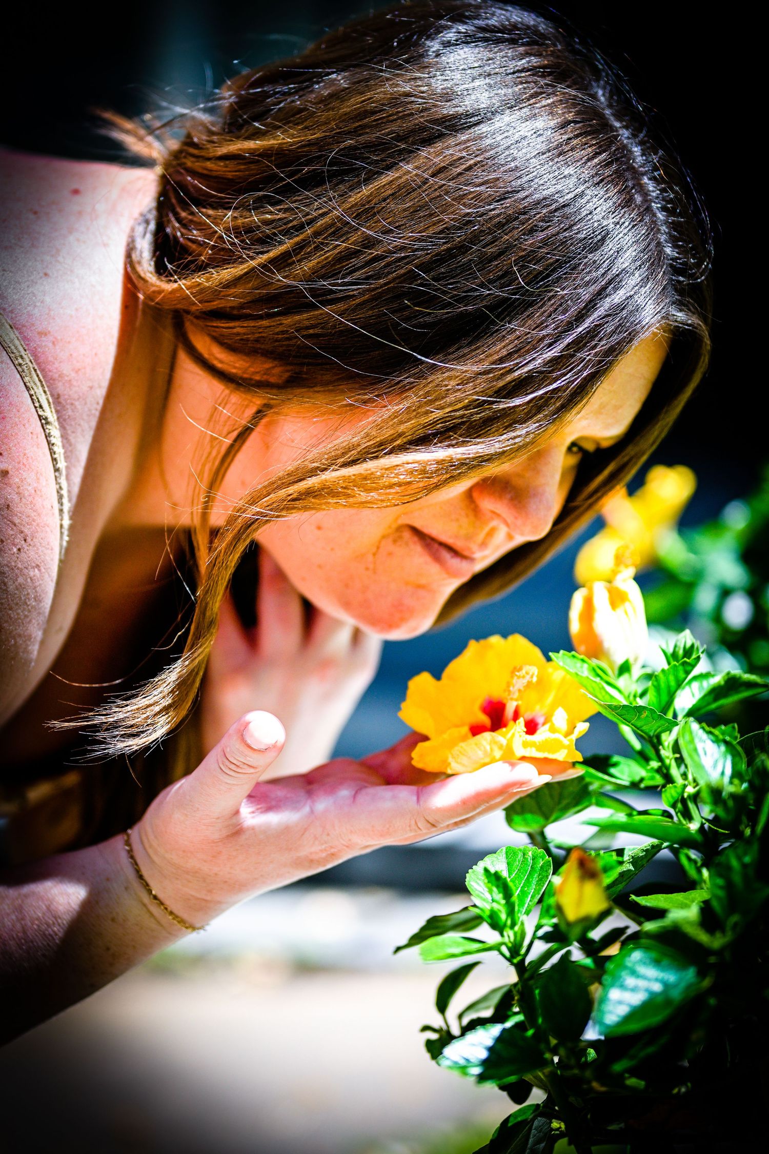 Close-up artistic photo series showing someone leaning in to smell bright yellow flowers against dark background.