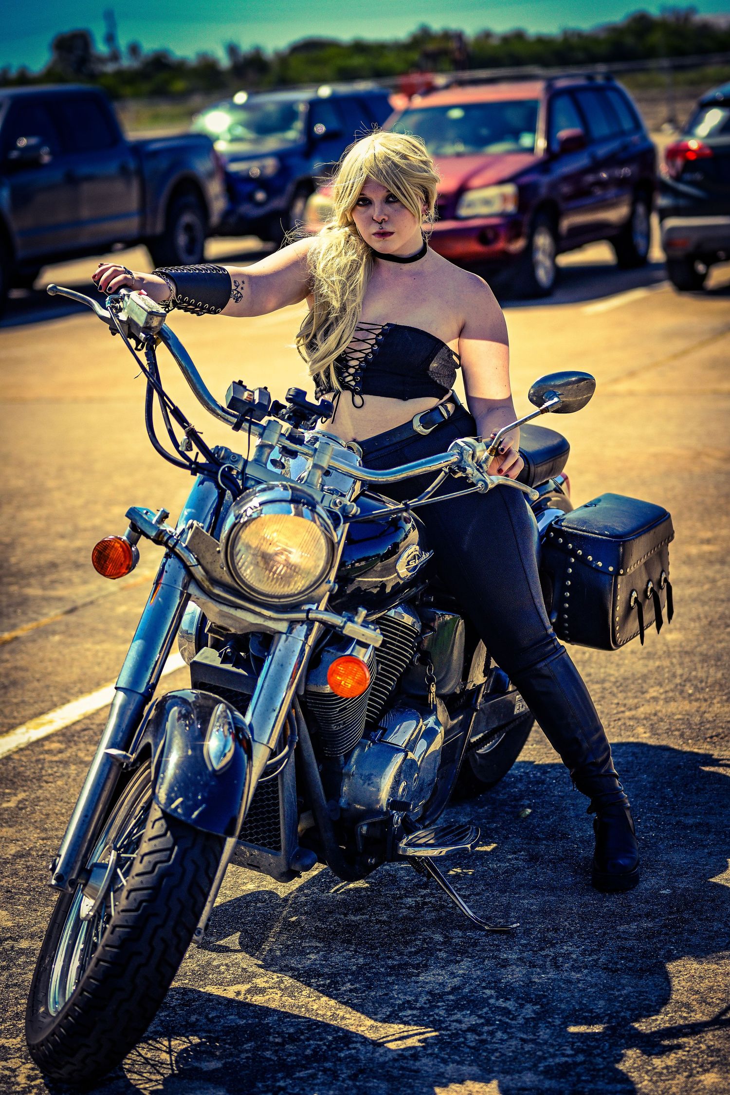 Cosplayer in black outfit poses on motorcycle in parking lot.