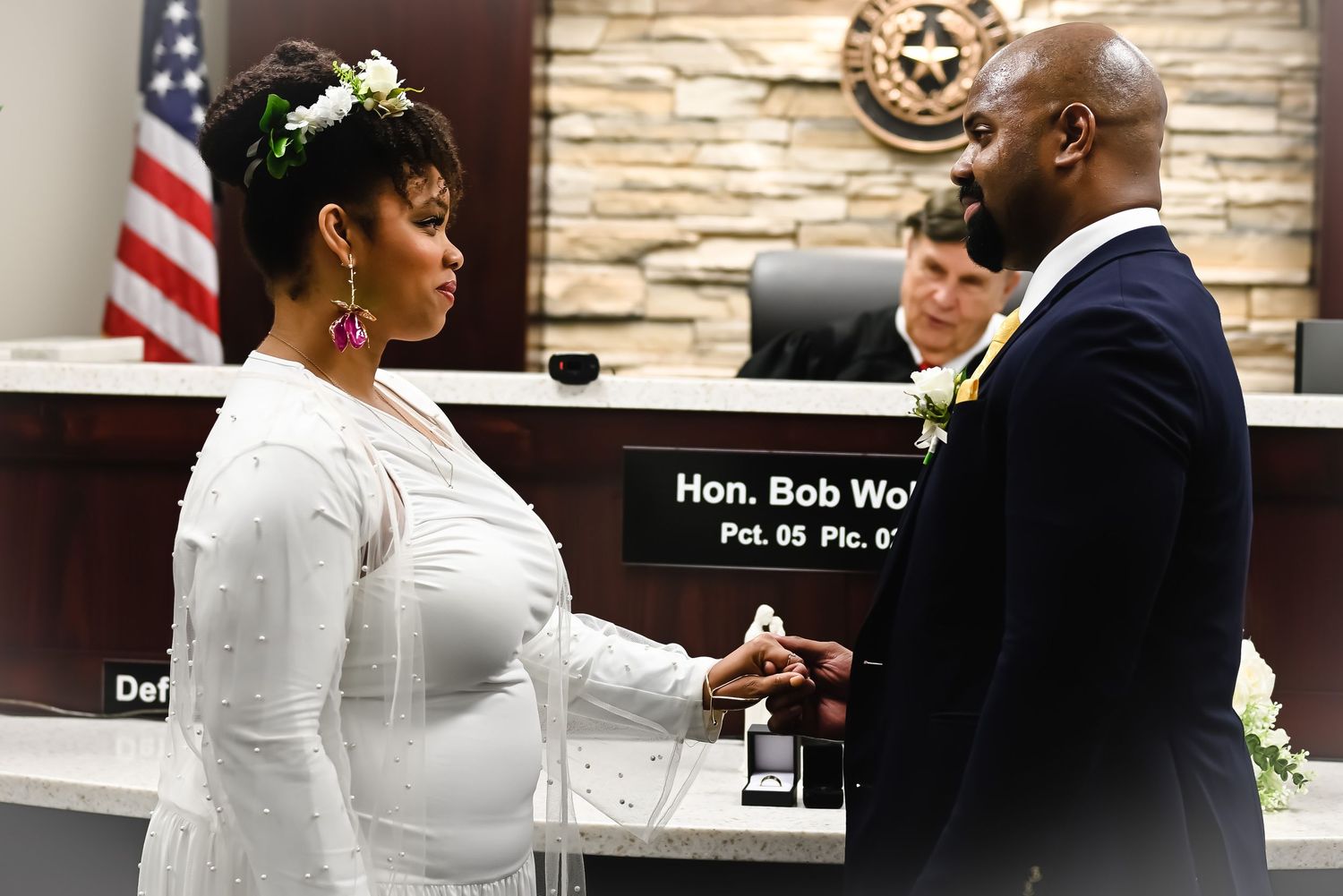 Wedding ceremony in a courthouse with American flag and stone wall backdrop.