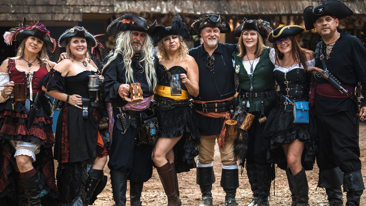 Group of steampunk cosplayers in pirate-themed outfits posing with drinks.