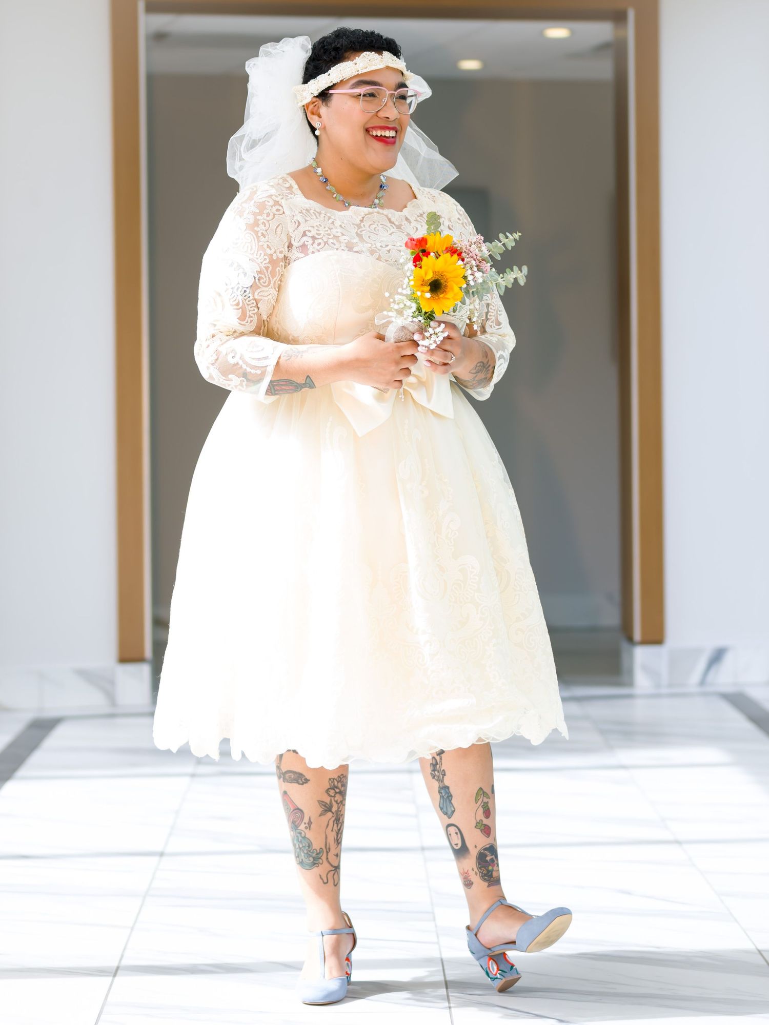Bride in a flowing white lace dress poses with yellow flowers.