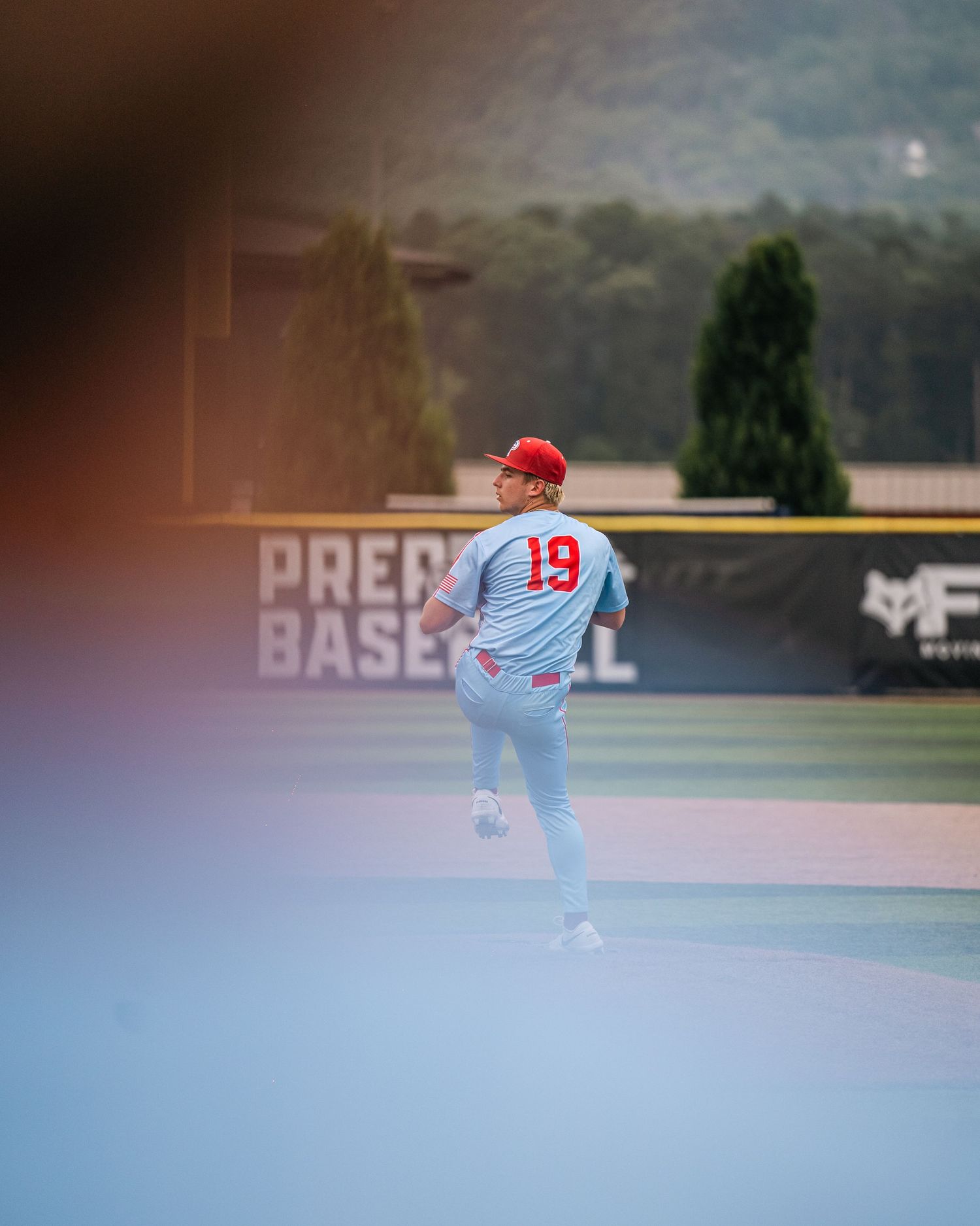 Baseball player #19 in red and white uniform runs on field near Prep Baseball sign.
