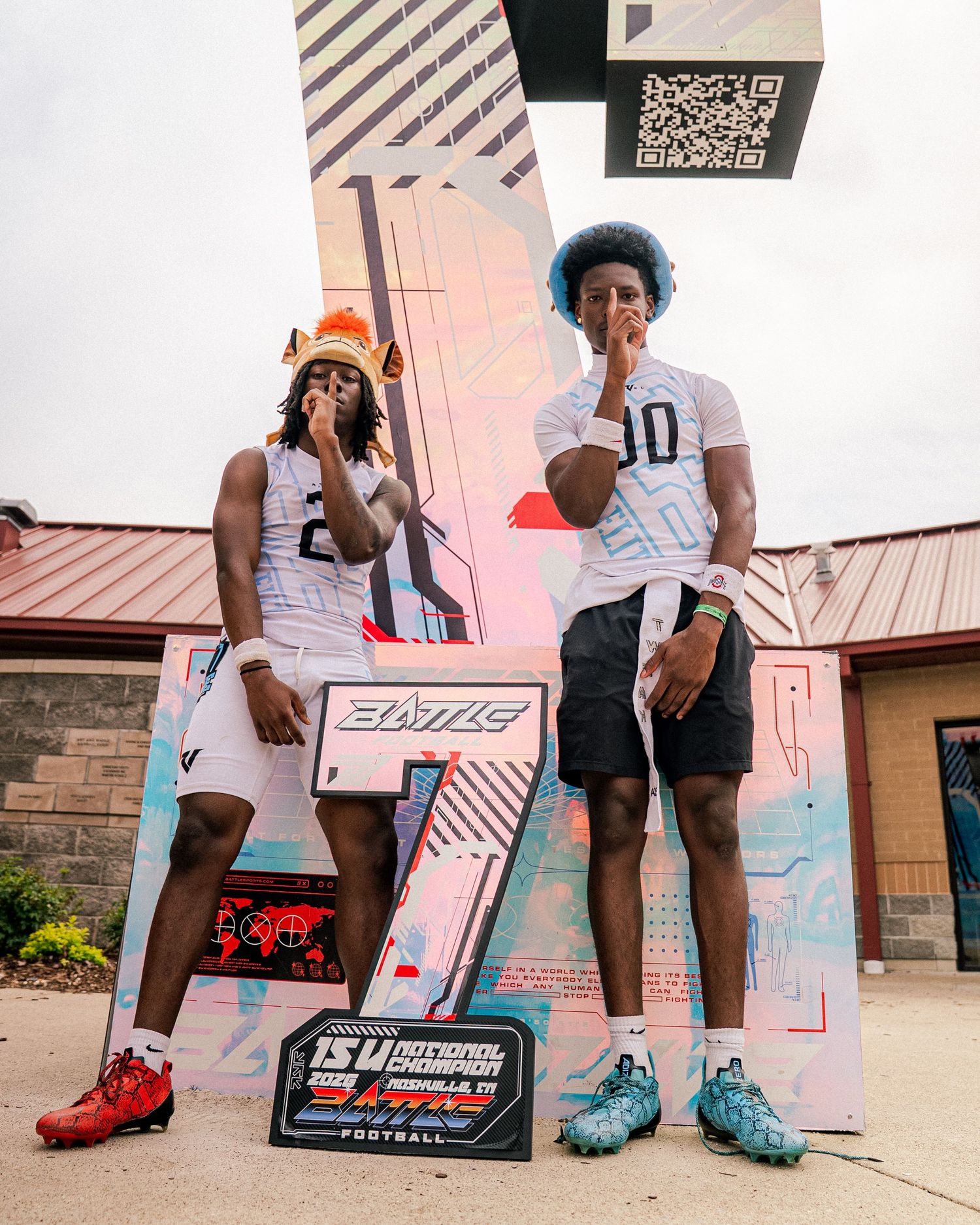 Two football players in white jerseys numbered 2 and 10 pose at a colorful 7S National Championship display.