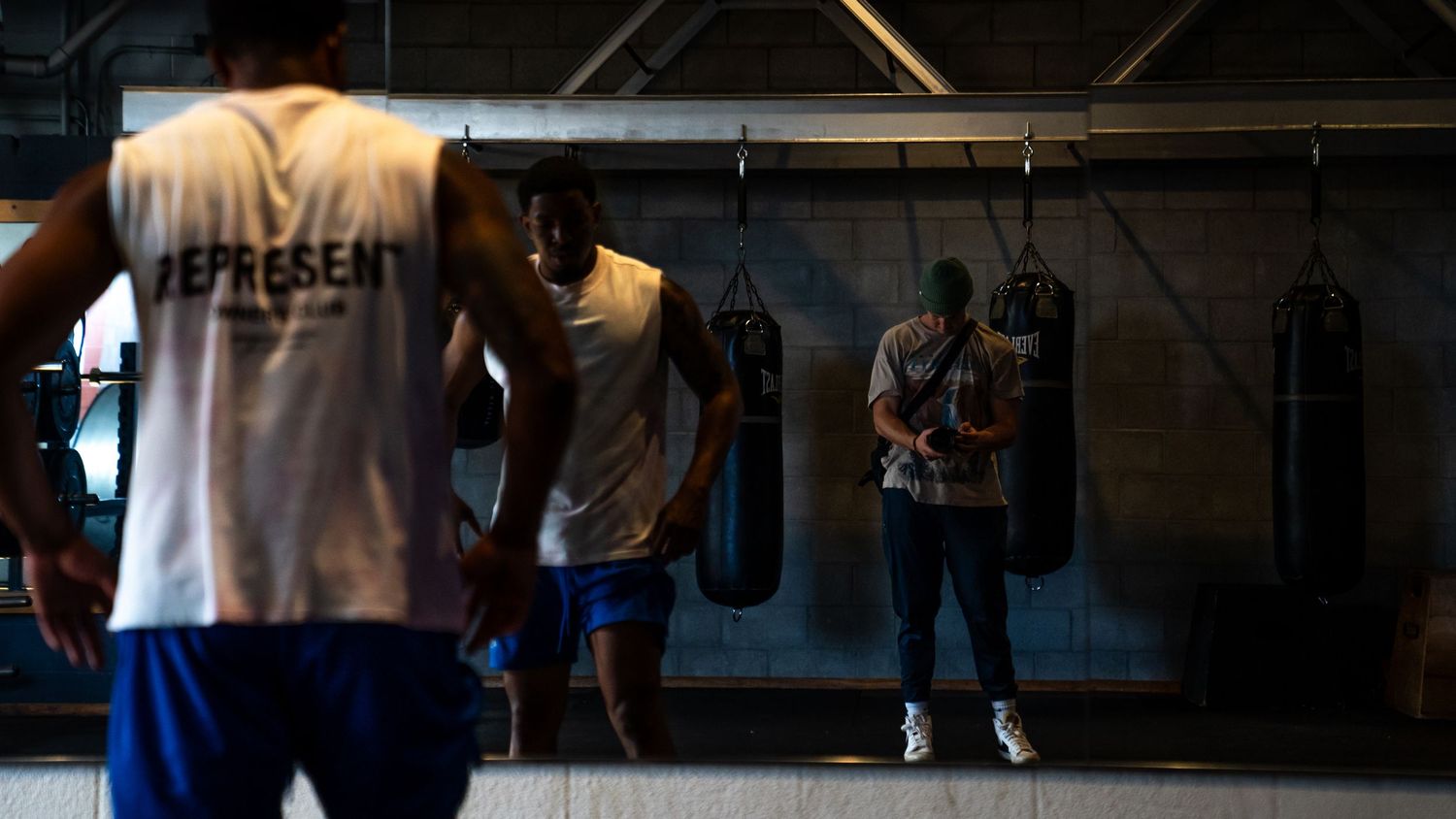 Athletes train in a dimly lit boxing gym with punching bags hanging from the ceiling.