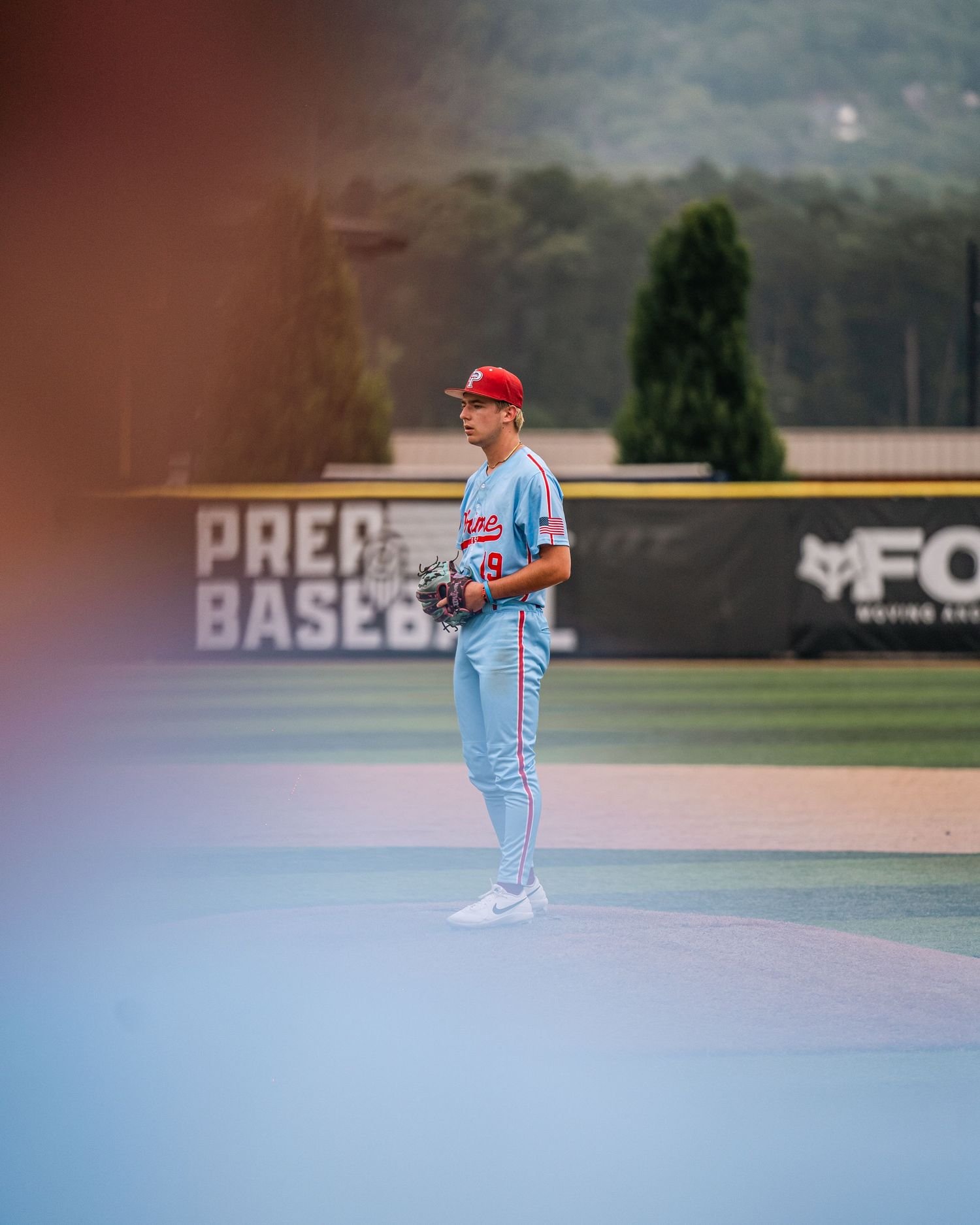 Baseball pitcher in light blue uniform standing on field at Prep Baseball showcase event.