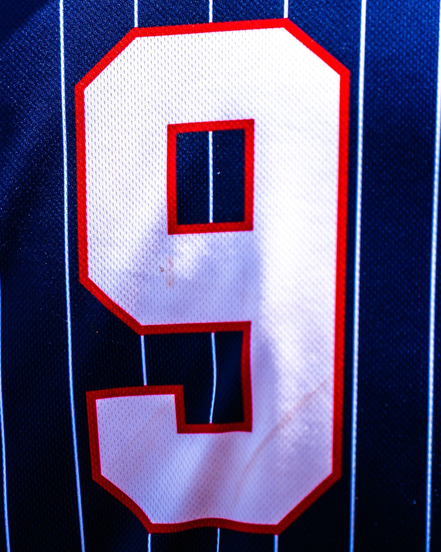 Close-up of a navy blue pinstripe sports jersey featuring the number 9 in white with red and black outline.