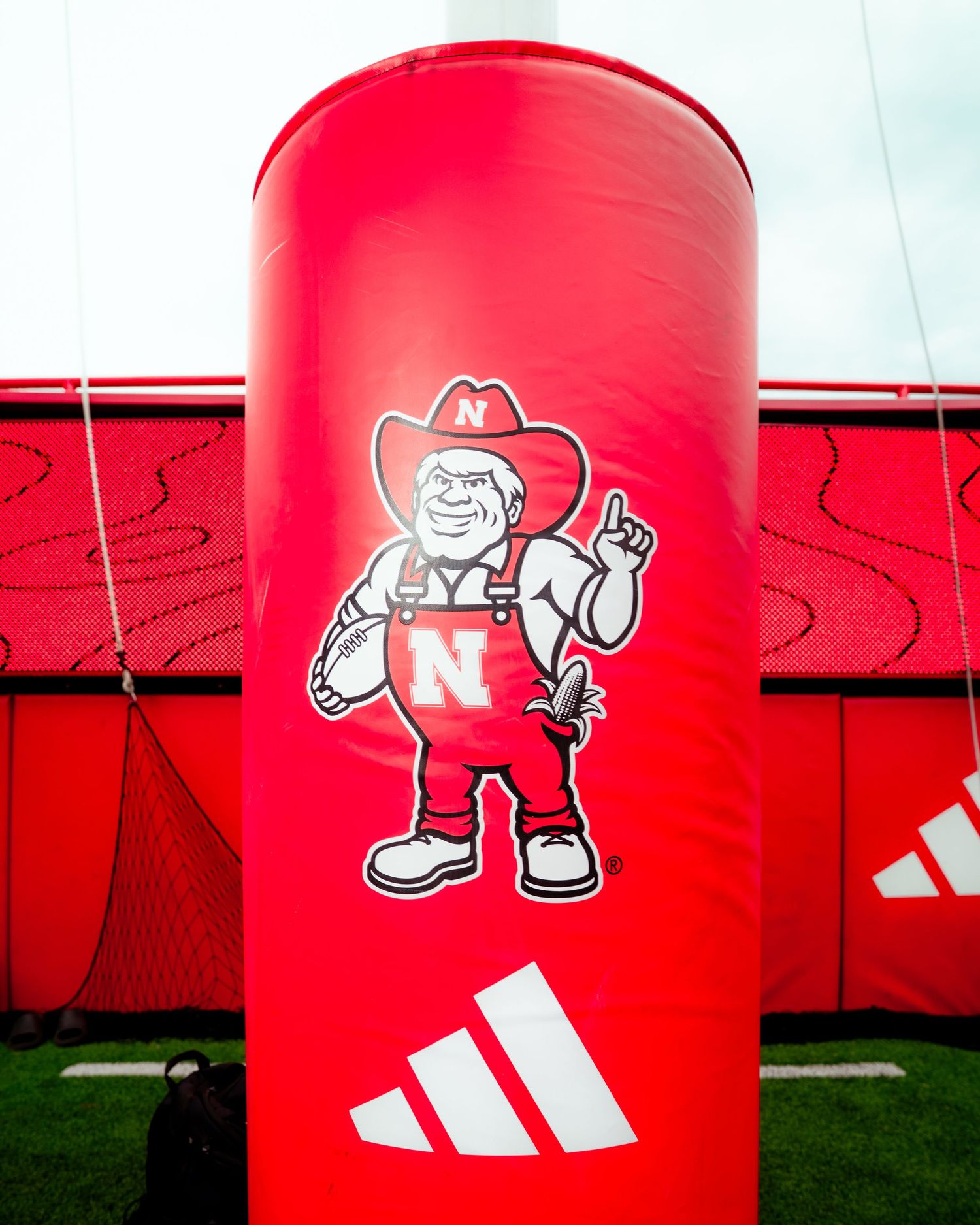 Red Adidas padded post featuring Nebraska Cornhuskers Herbie Husker mascot logo at football training facility.
