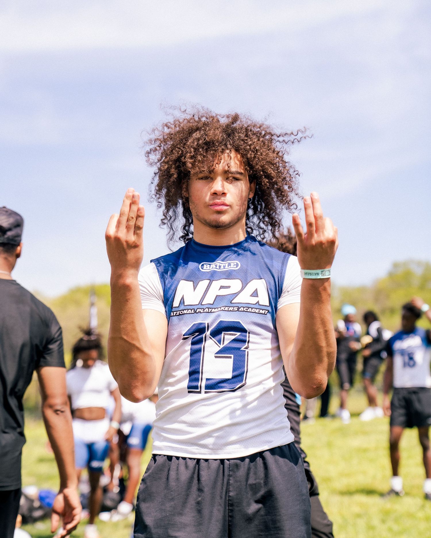 Young athlete wearing NPA jersey number 13 poses outdoors at a football training camp on a sunny day.