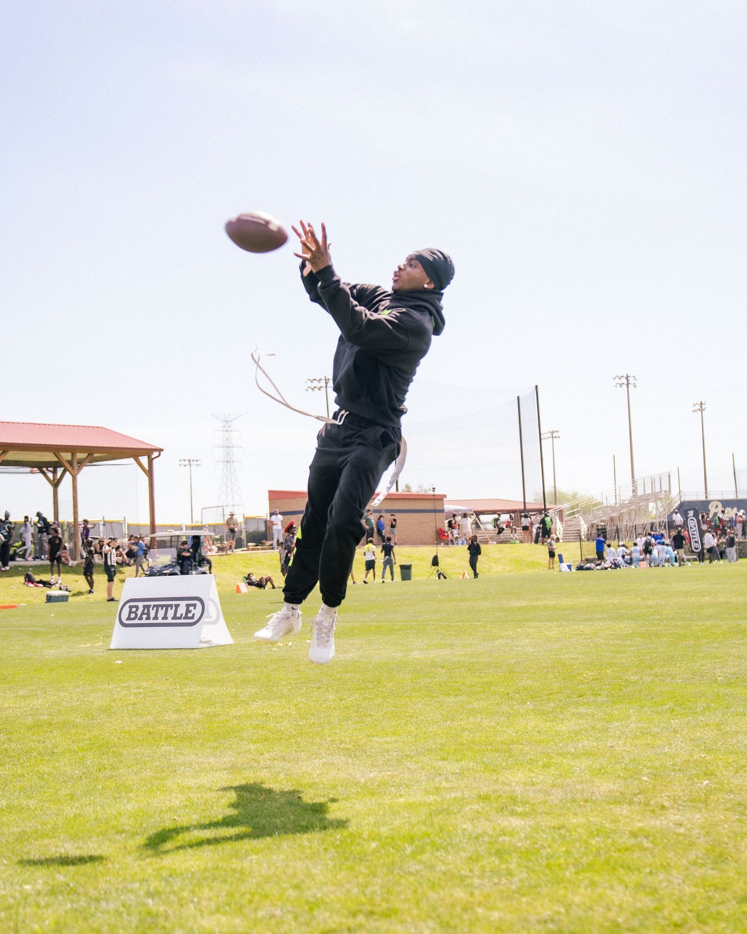 Athlete leaping to catch a football at an outdoor Battle sports event on a green field.