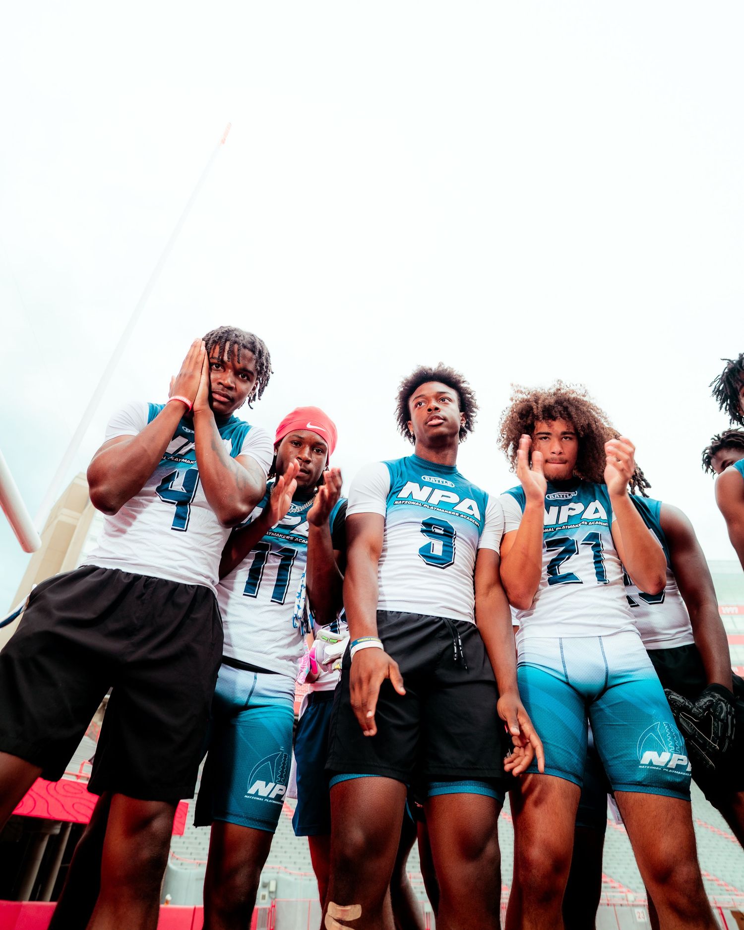 Young athletes in NPA teal and white uniforms huddle together on a sports field during a competitive event.