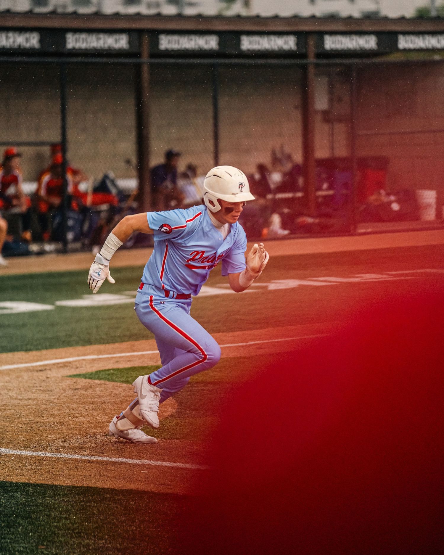 Baseball player in light blue uniform sprints the bases during a game with BODYARMOR signage visible.