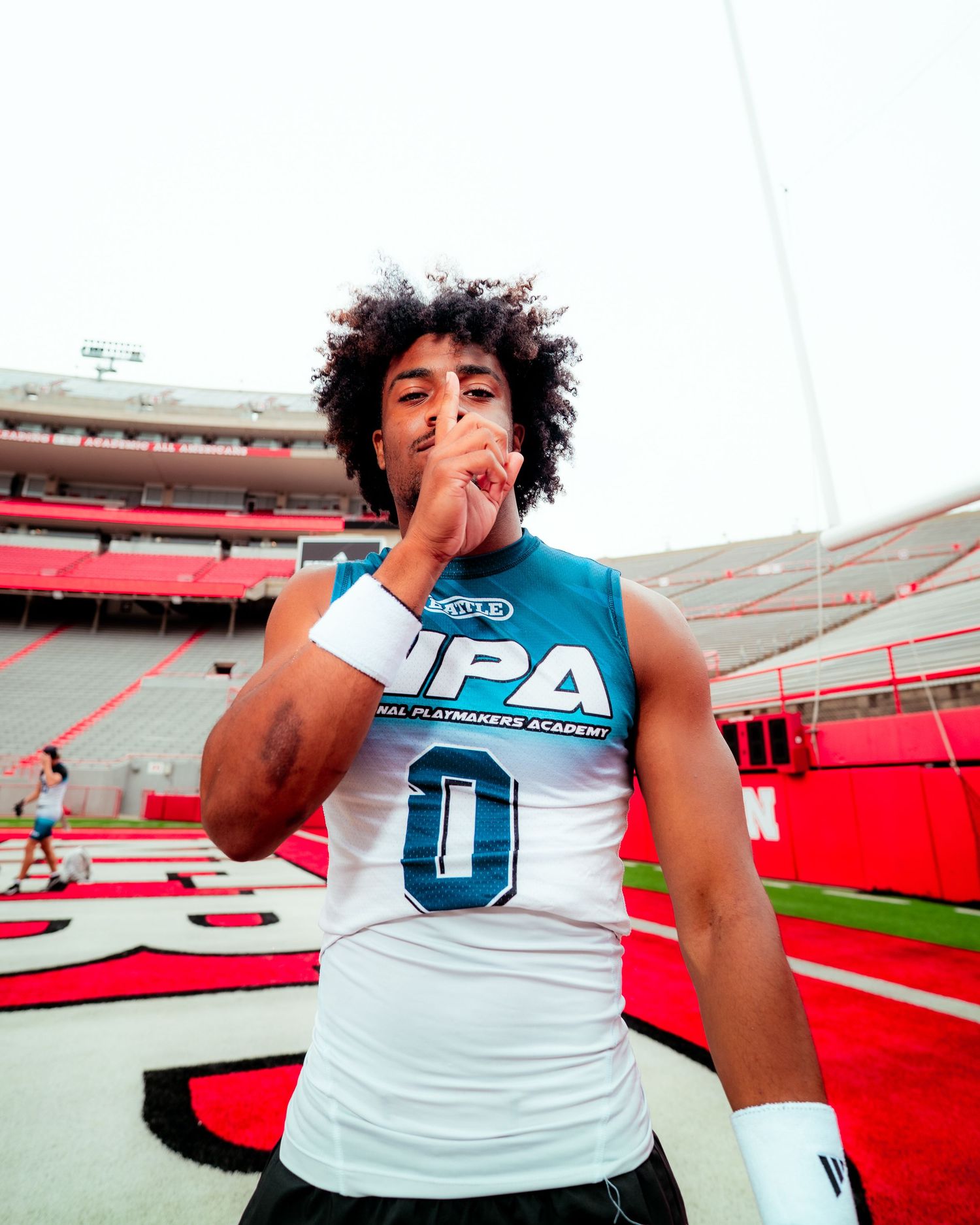 Young athlete in UPA jersey number 0 poses on football field in large stadium with red seating.