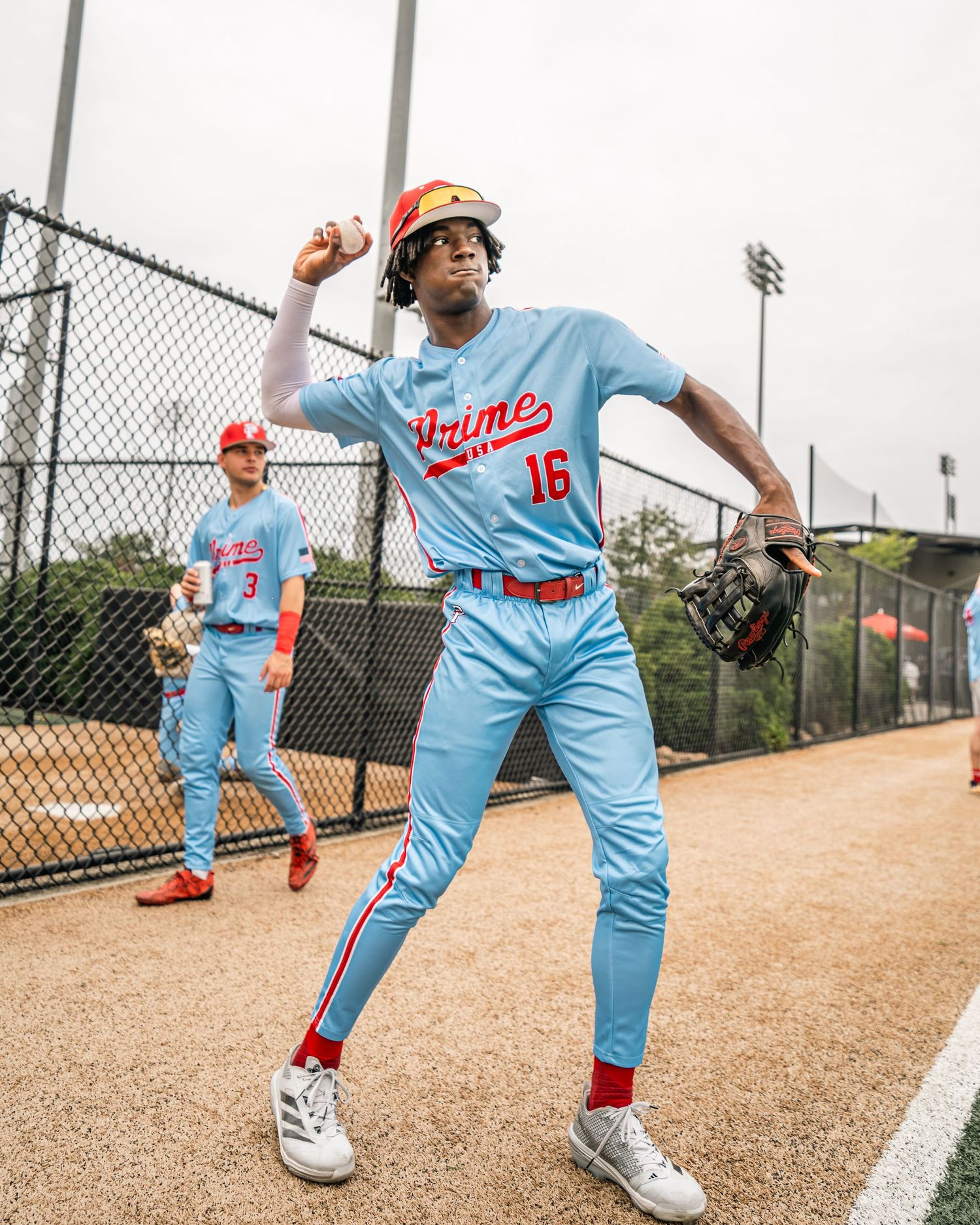 Baseball player #16 in light blue Prime uniform throwing ball during warm-ups on dirt field.