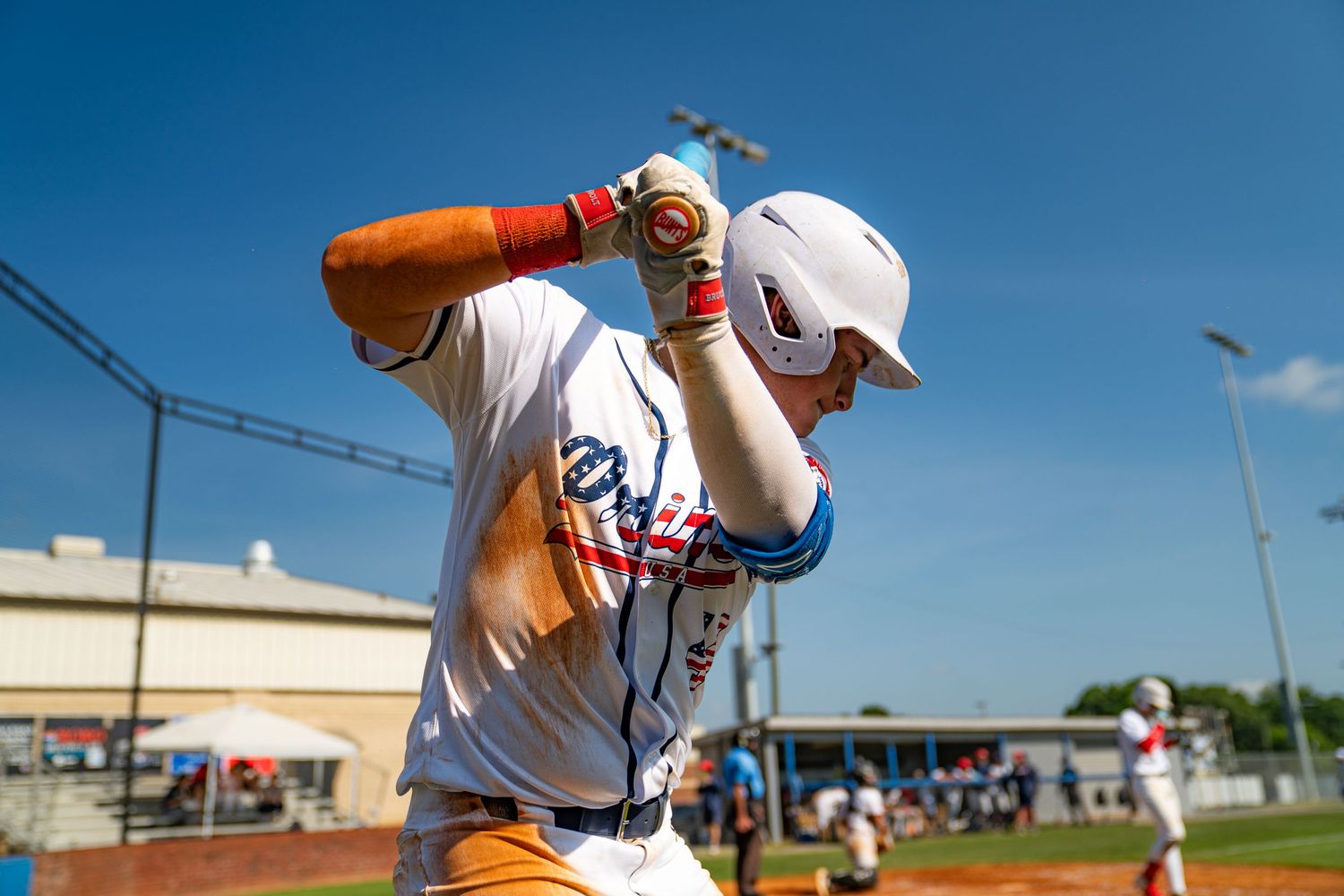 Baseball player in white uniform adjusting helmet on sunny day at outdoor baseball field.