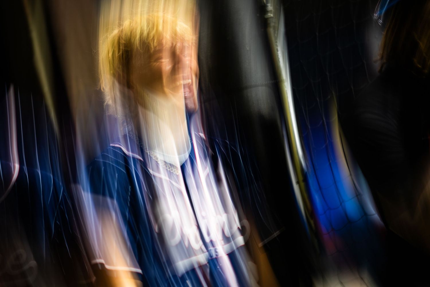 Blurred motion portrait of a blonde woman in a blue jacket, creating an artistic abstract effect with streaks of light.