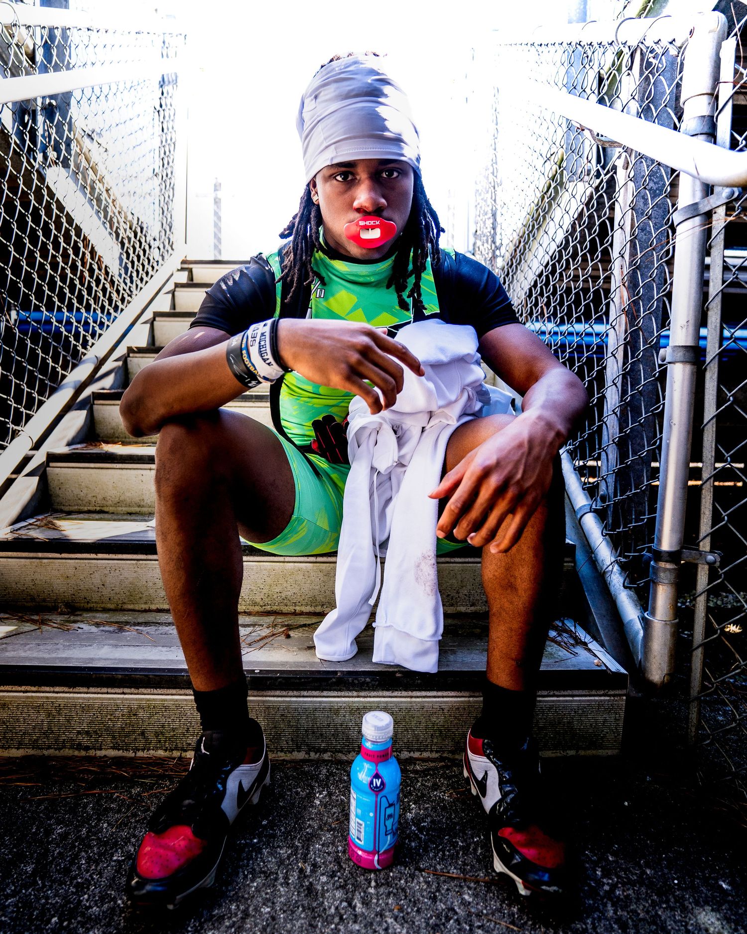 Athlete in green outfit and head wrap sits on stairs, holding white socks with a water bottle nearby.