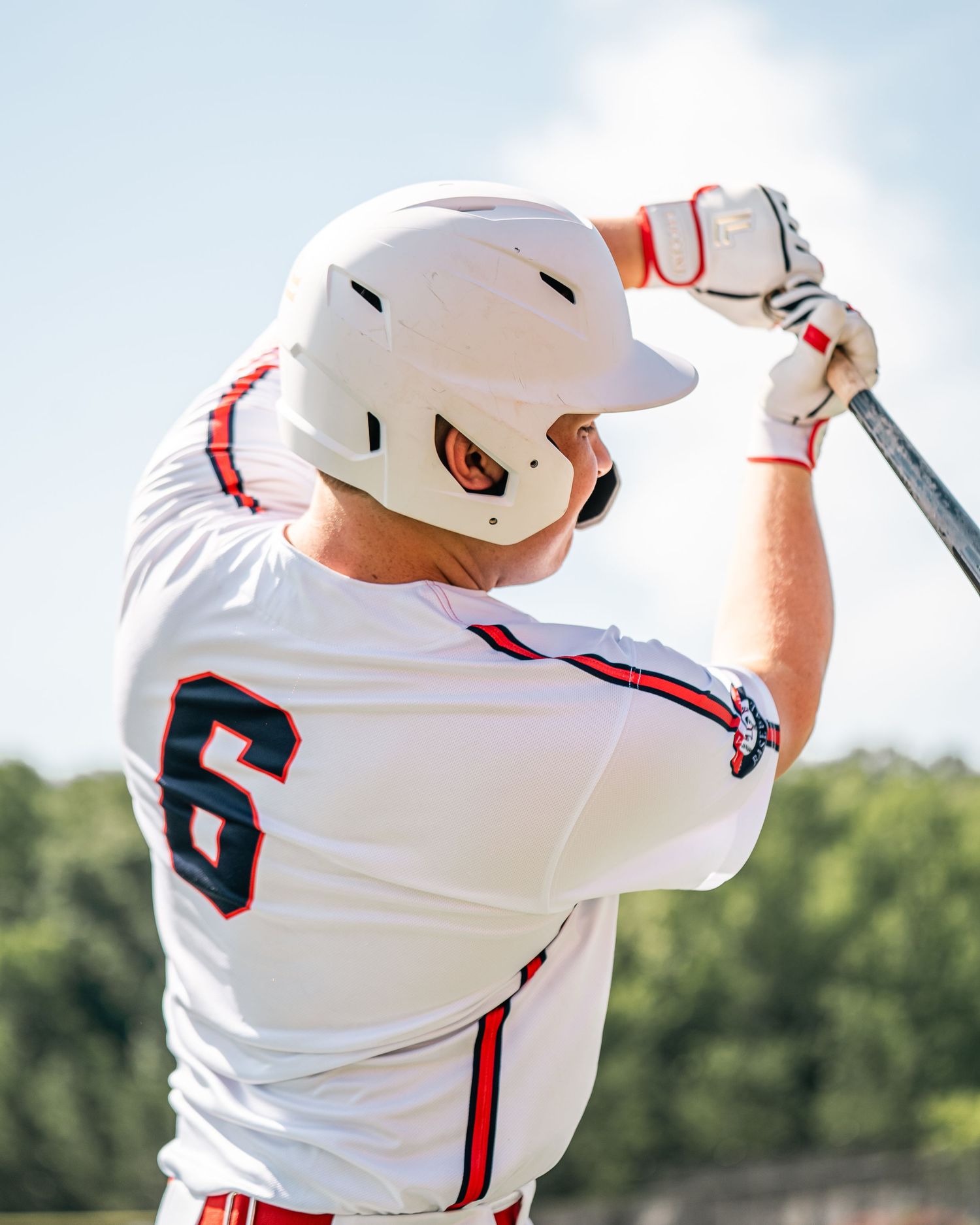 Baseball player wearing number 6 white uniform and helmet swings bat during a sunny outdoor game.