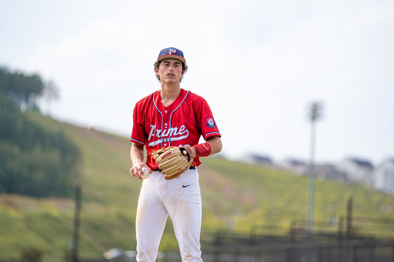 Young baseball player in red Prime jersey holding glove on field during game.