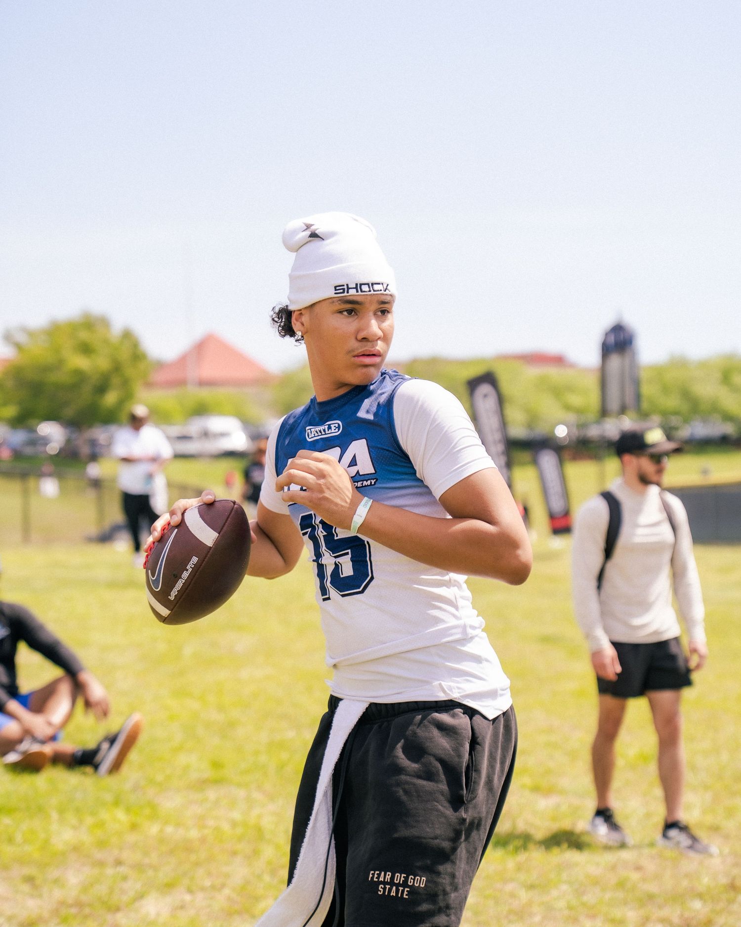 Young quarterback in white SHOCK jersey preparing to throw football at outdoor camp event.
