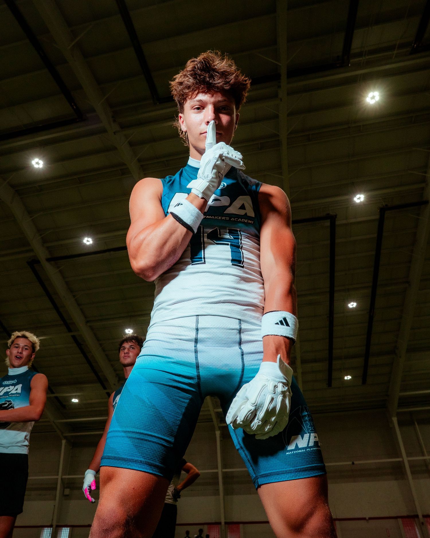 Athletic male pole vaulter in blue compression shorts and gloves poses indoors at a track and field event.