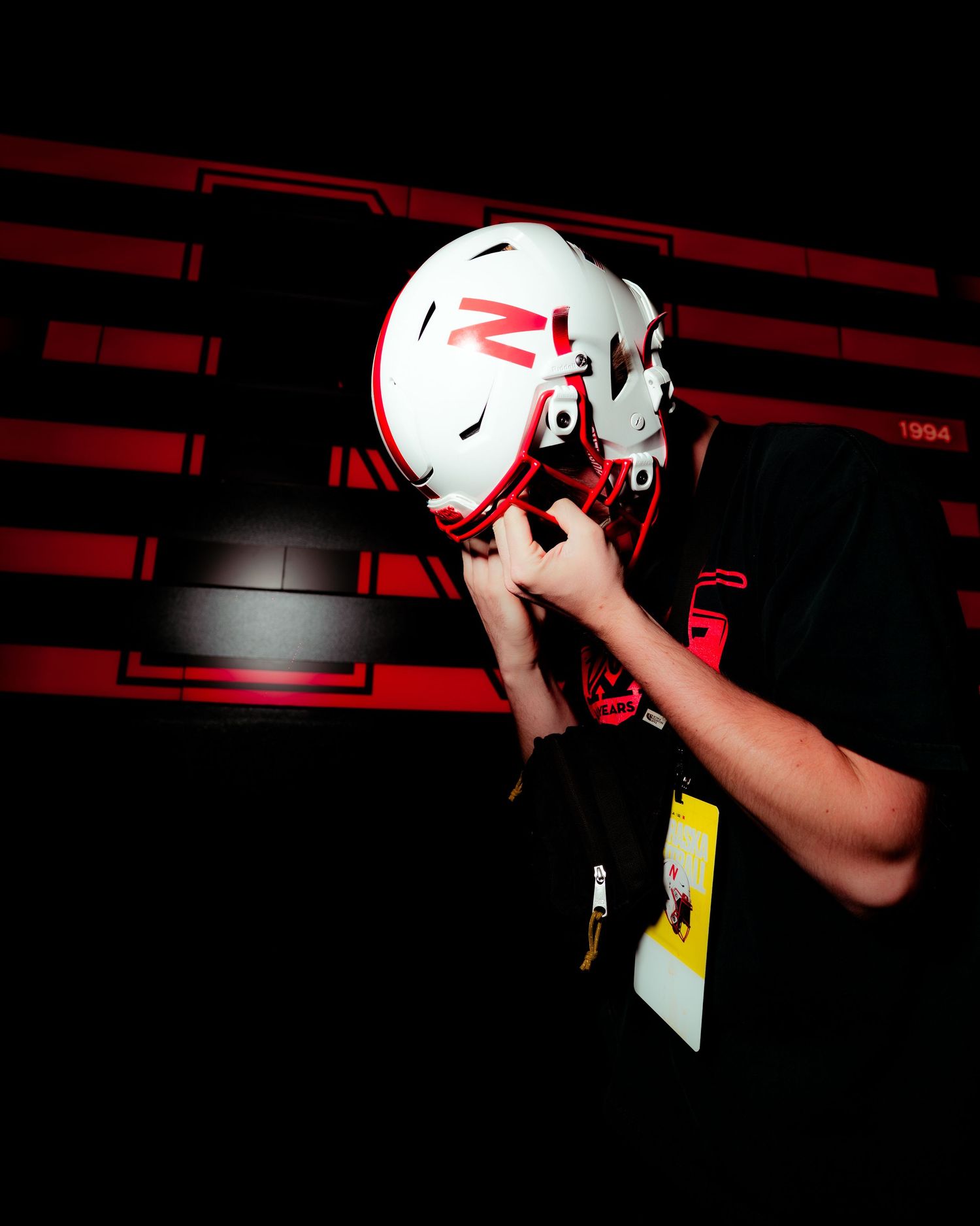 Person trying on a white and red football helmet with face mask in a dimly lit red-themed display room.