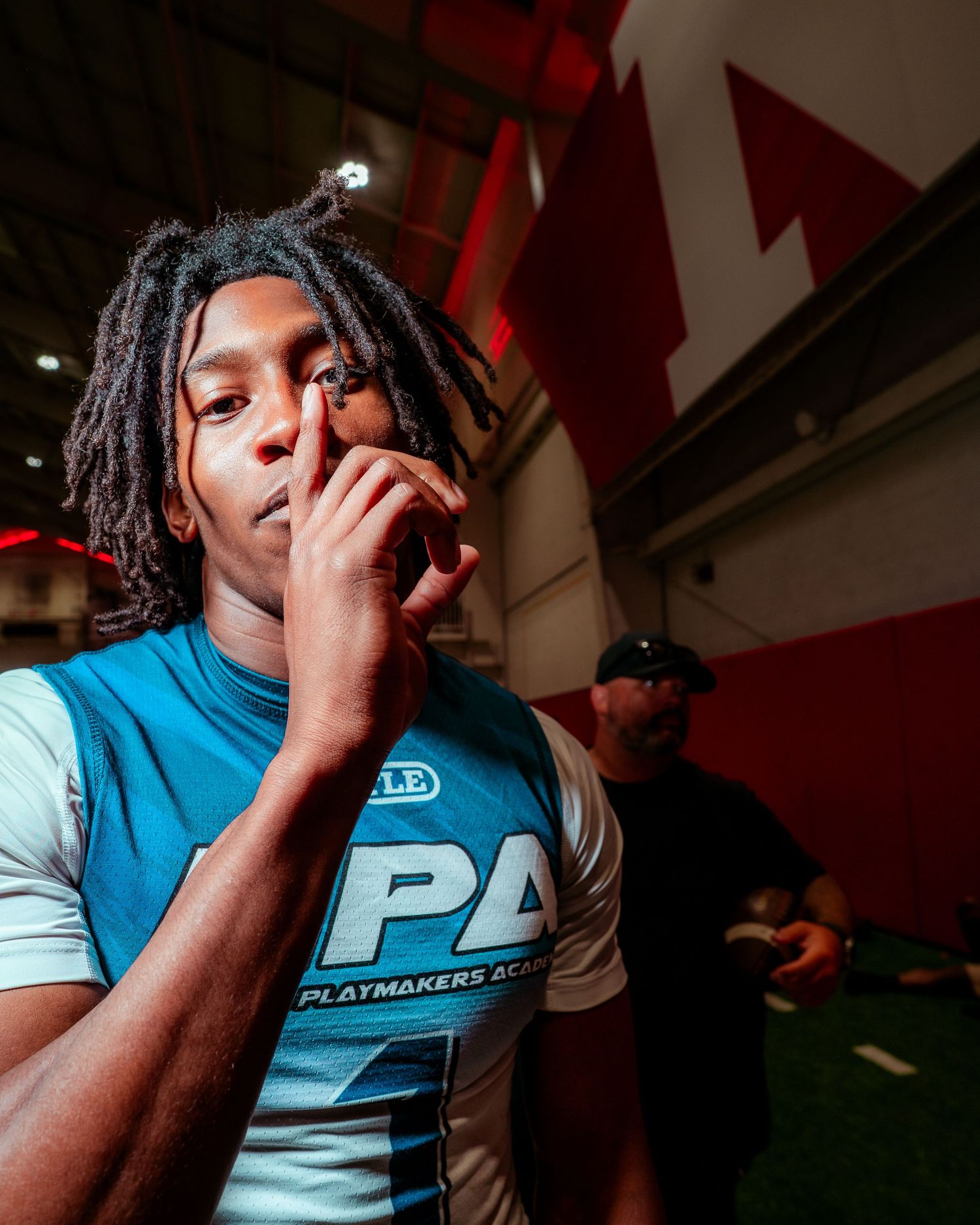 Young athlete in Playmakers Academy jersey poses thoughtfully indoors at sports facility.