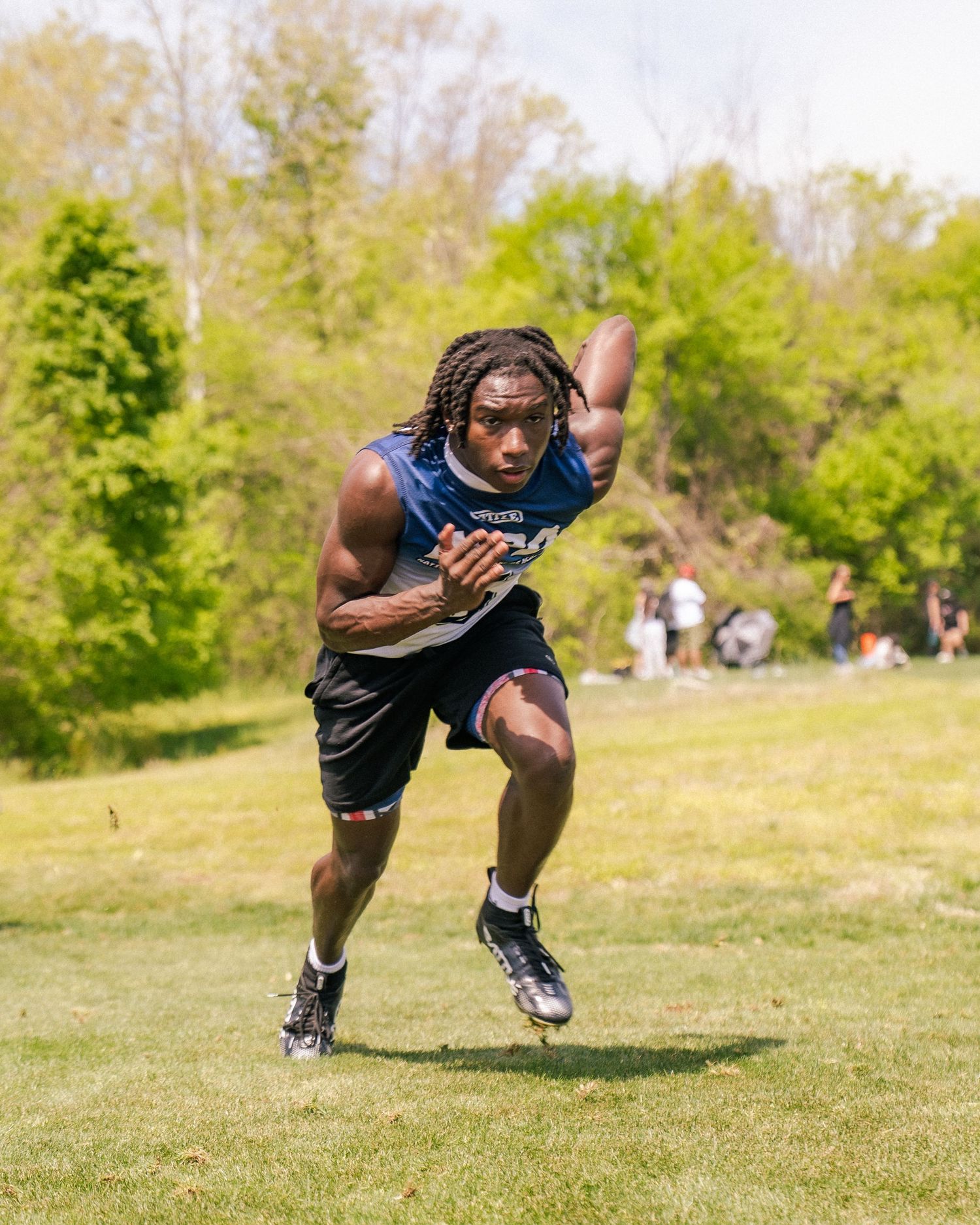 A muscular football player in blue uniform sprints across a green field during an outdoor training session.