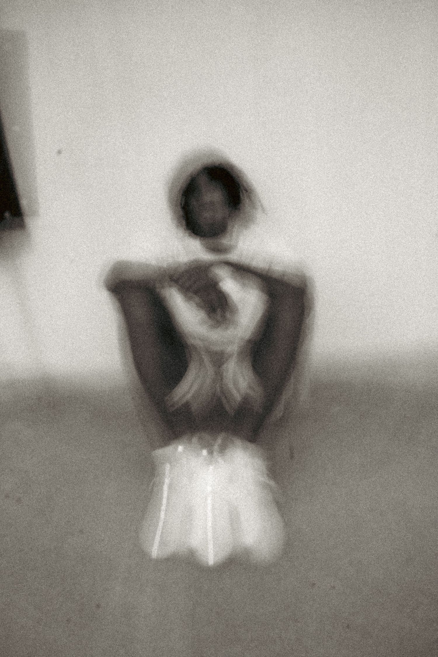 Blurry black and white photo of a person kneeling with arms crossed behind their back in an artistic pose.