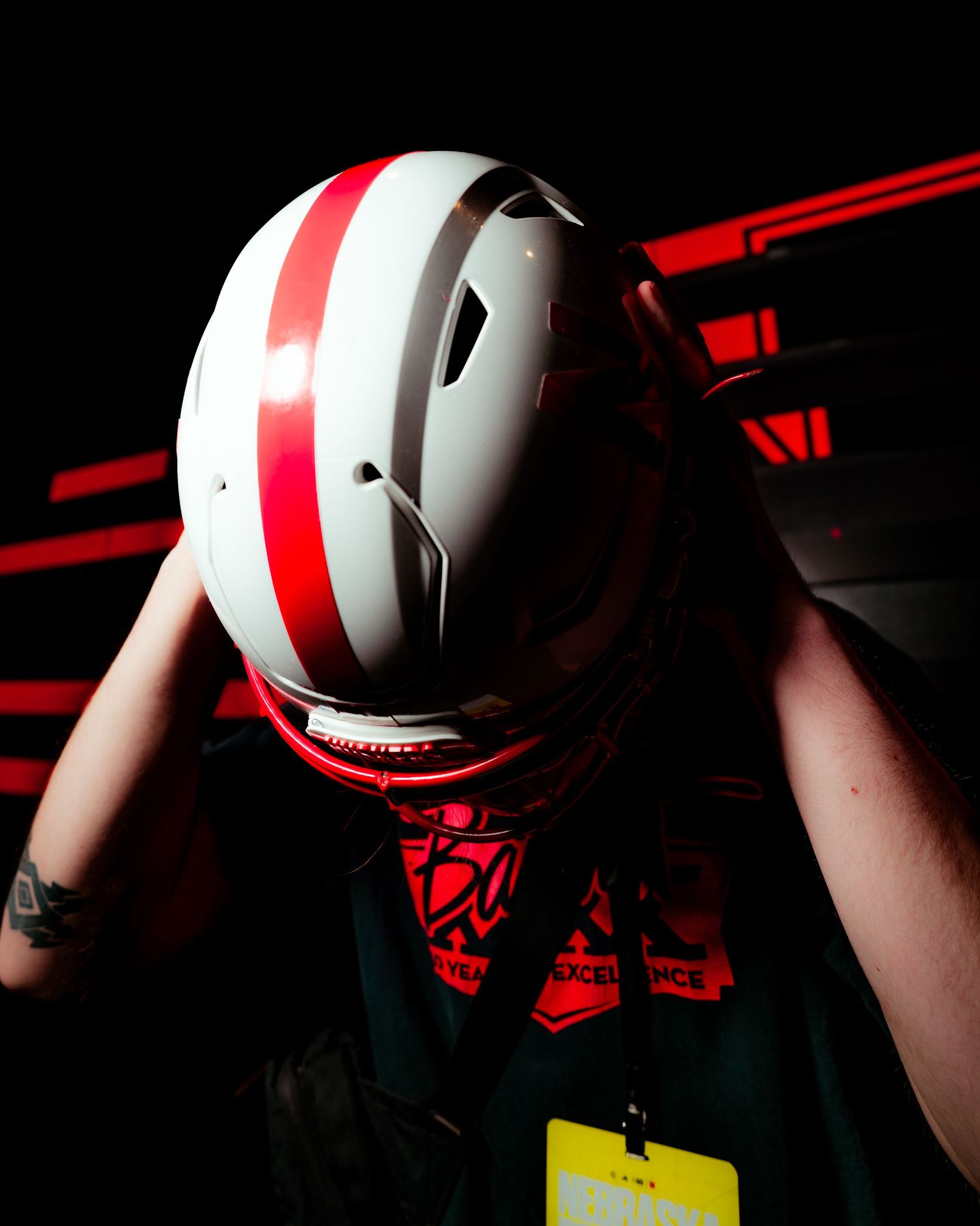 Person wearing a white and red striped motorcycle helmet in dramatic red-lit environment with yellow lanyard visible.