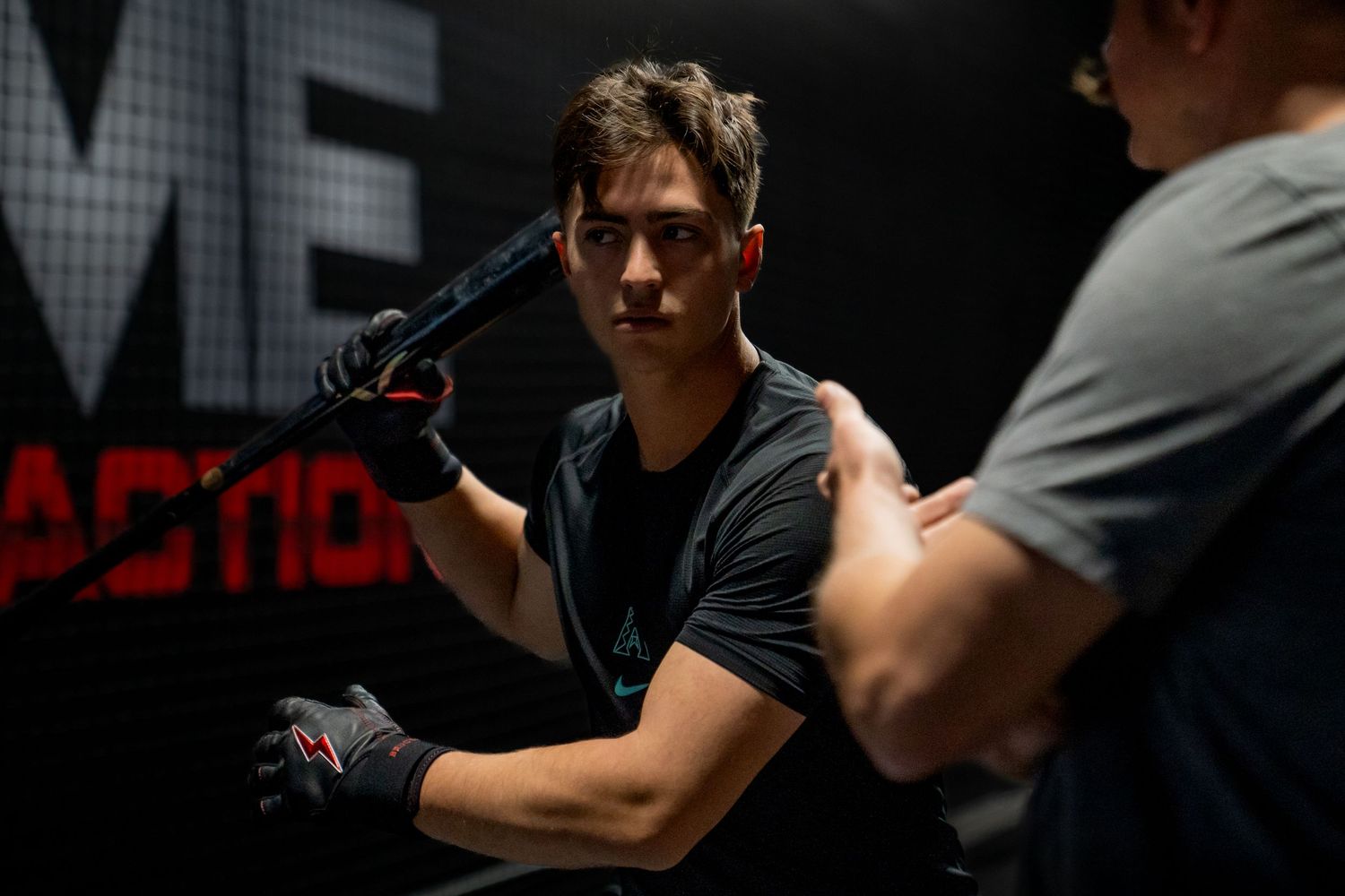 Young male martial artist in black training gear practices striking techniques in a dark gym.