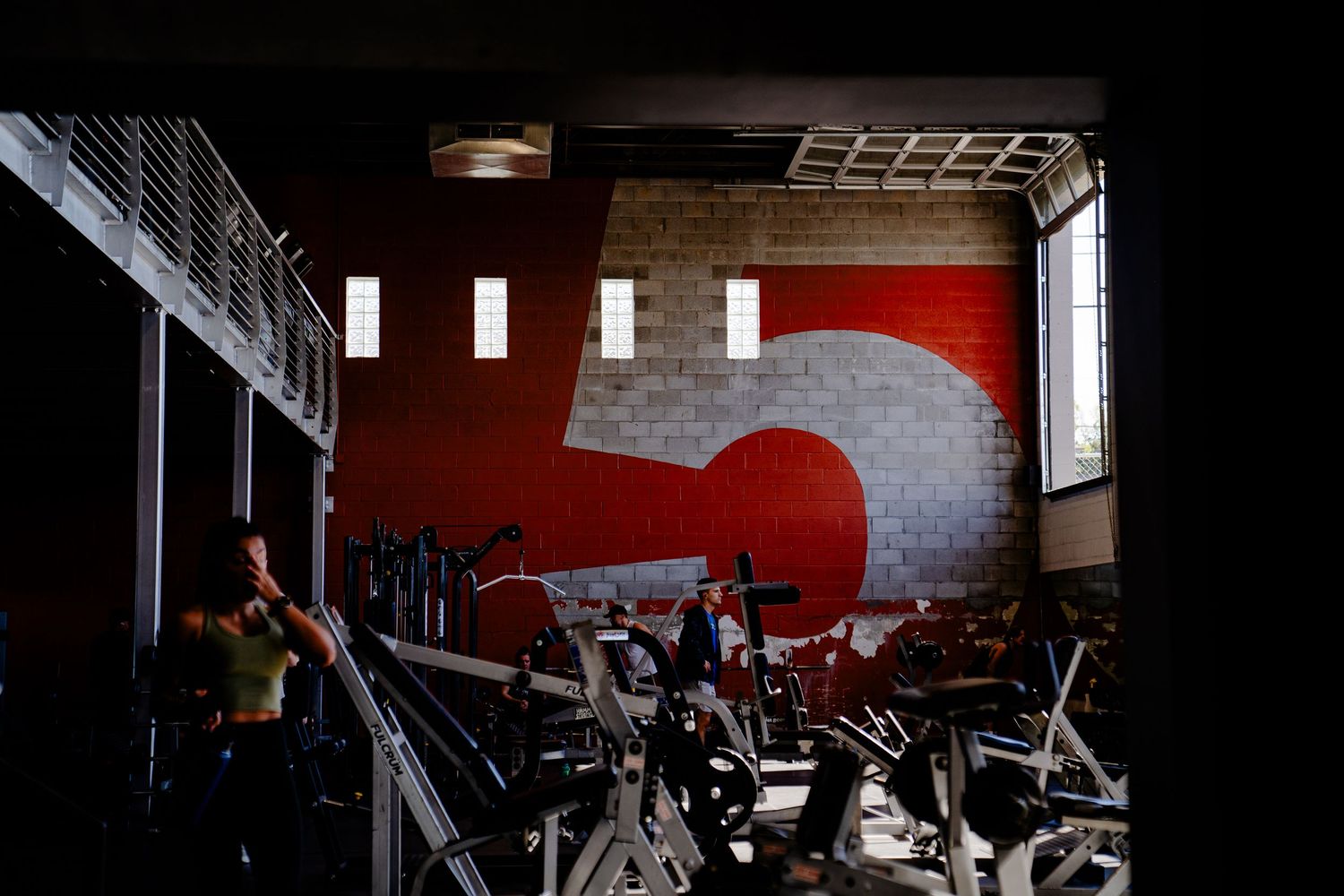 A dark gym interior with exercise equipment and a red accent wall visible in the lighting.