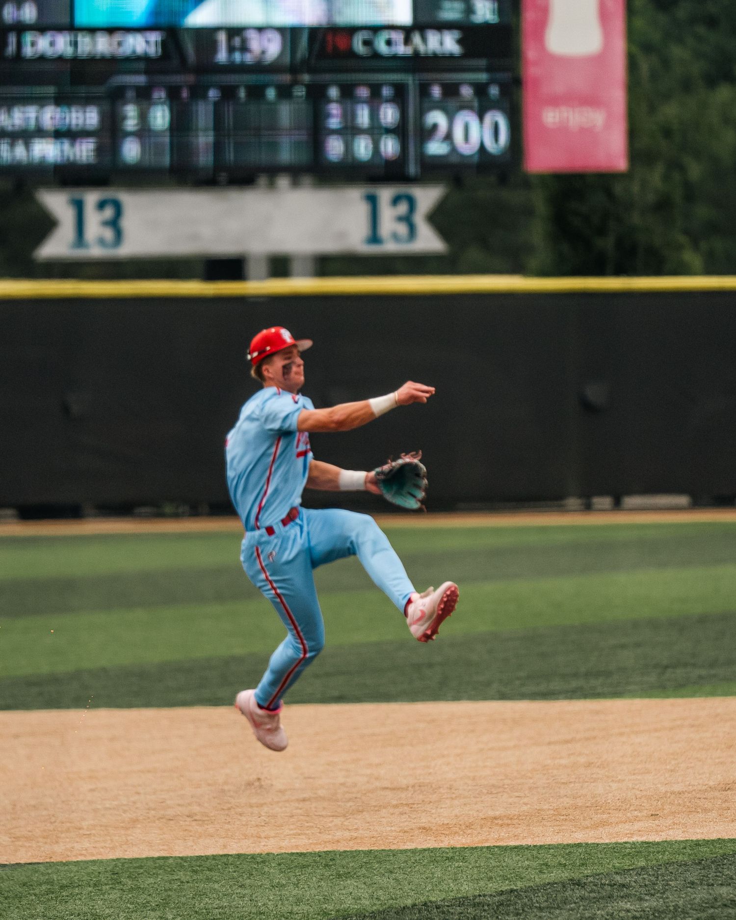 Baseball player in light blue uniform leaping mid-air while throwing ball during game.