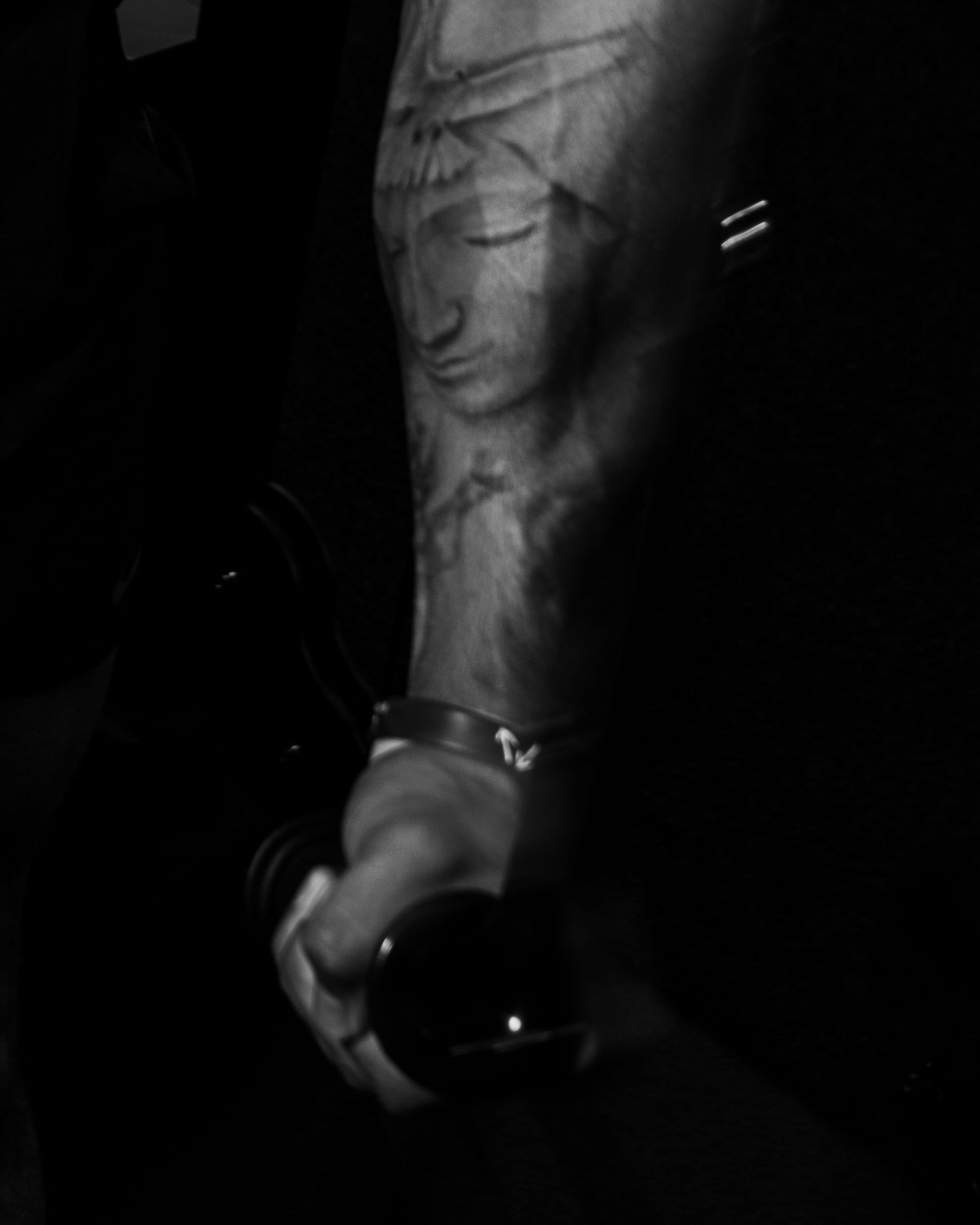 Black and white photo of a tattooed arm holding a dark glass sphere, wearing a silver bracelet.