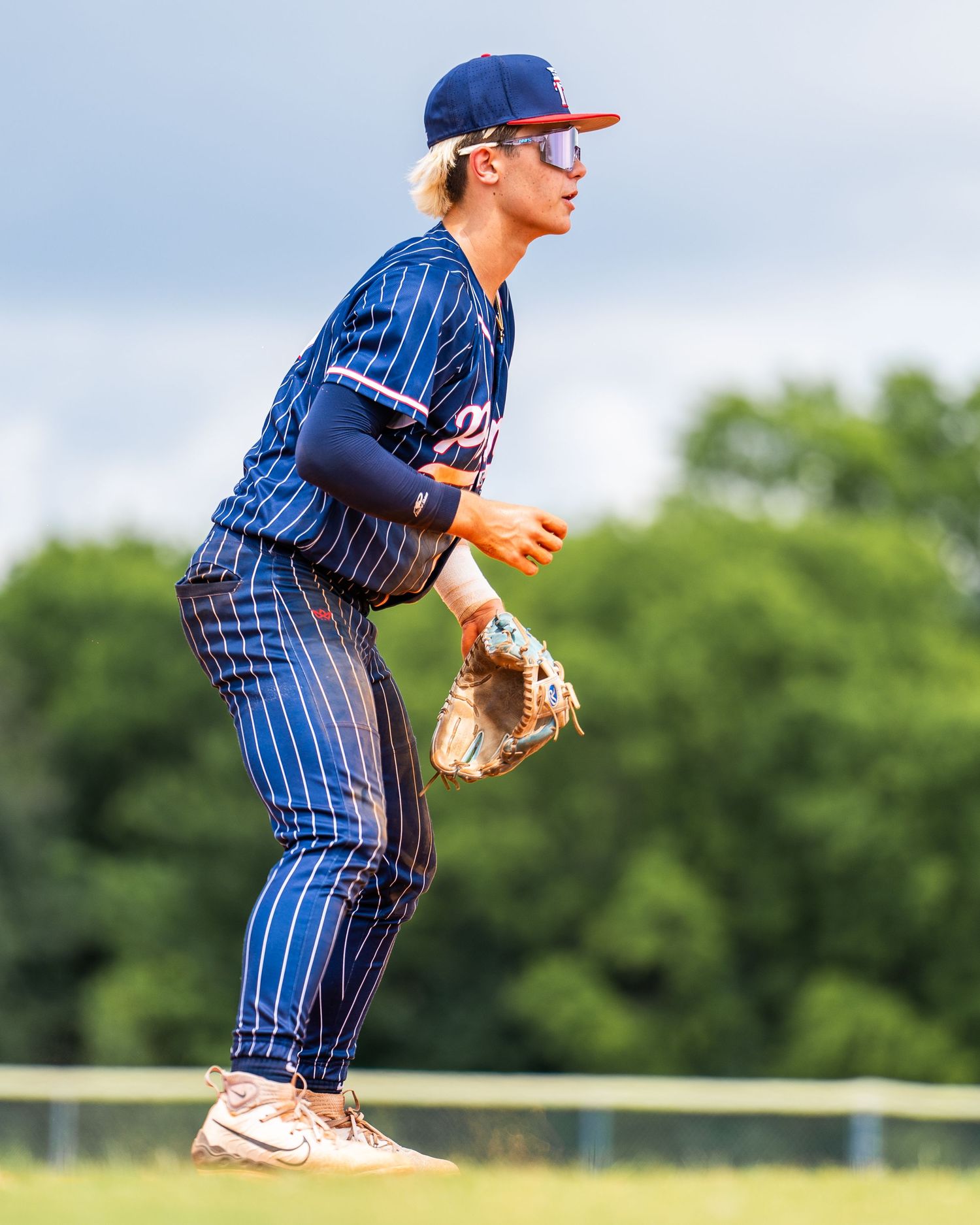 Baseball player in navy pinstripe uniform ready in fielding stance on green outfield grass.