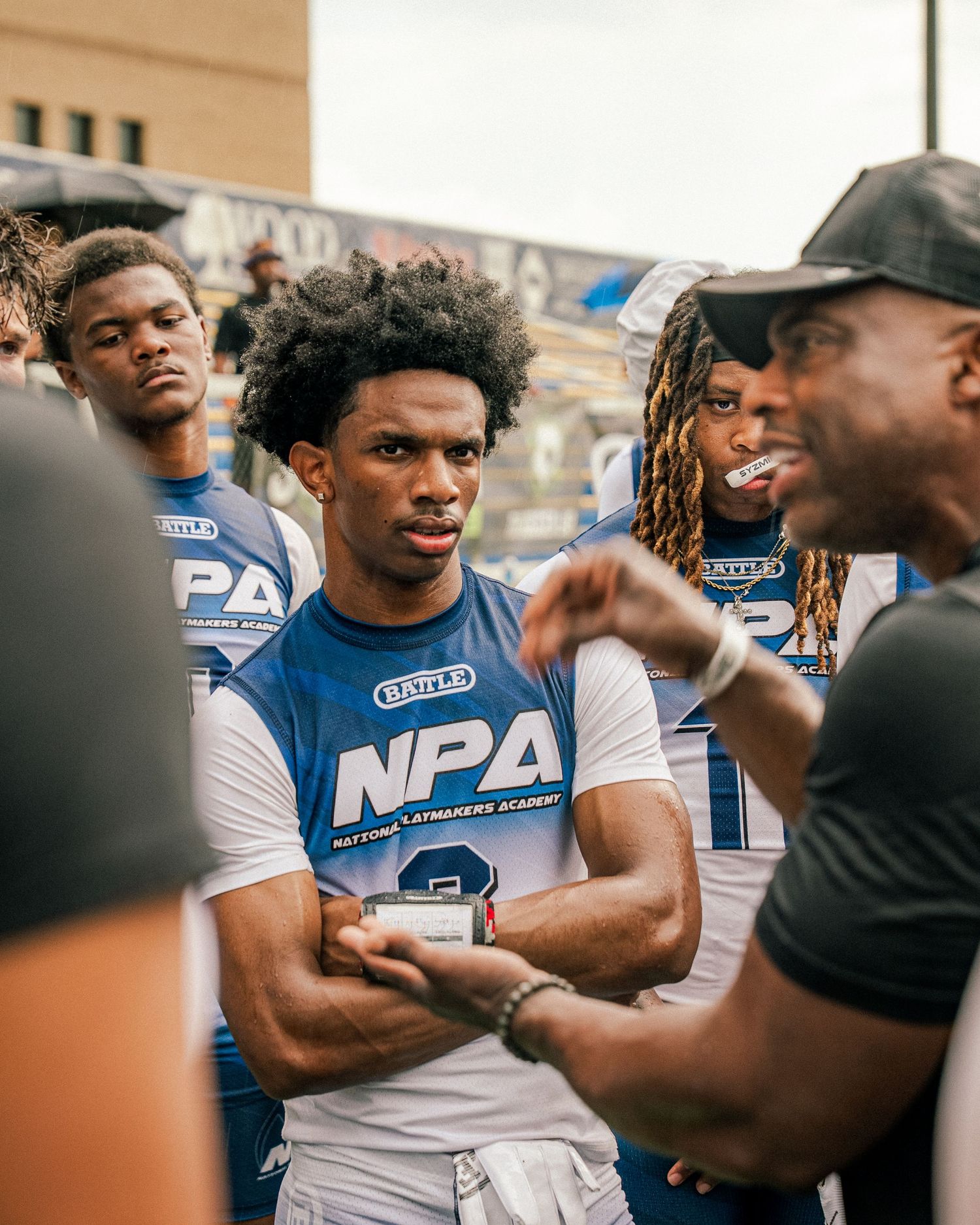 Young athletes in NPA jerseys listening to coach at National Playmakers Academy football camp.