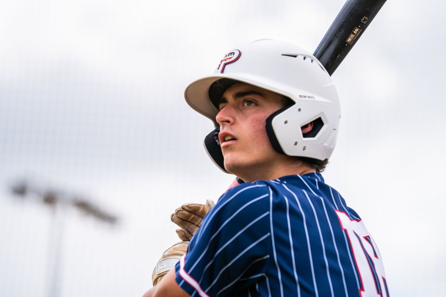 Young baseball batter in white helmet and navy pinstripe jersey holds bat ready at plate.