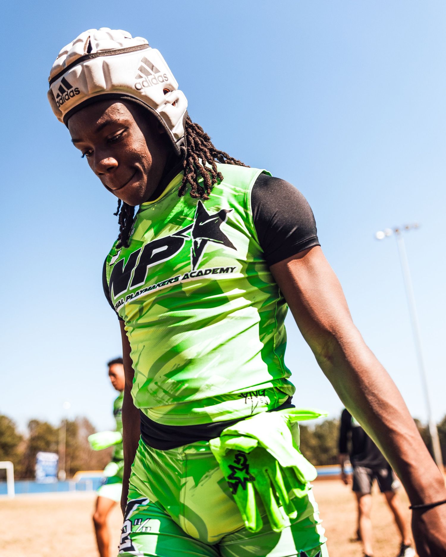 Young athlete in green WP Academy jersey and helmet playing flag football on sunny outdoor field.