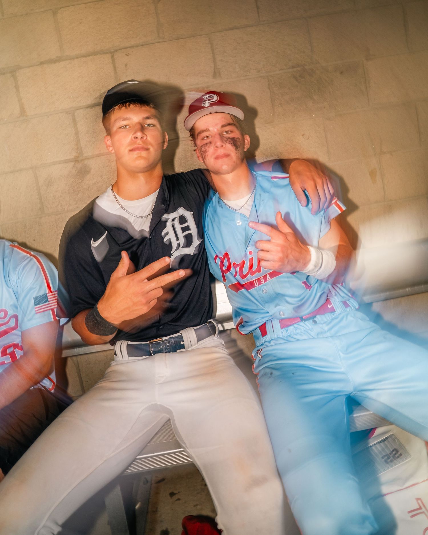 Two young baseball players in Detroit Tigers and Princeton uniforms pose together in a dugout.