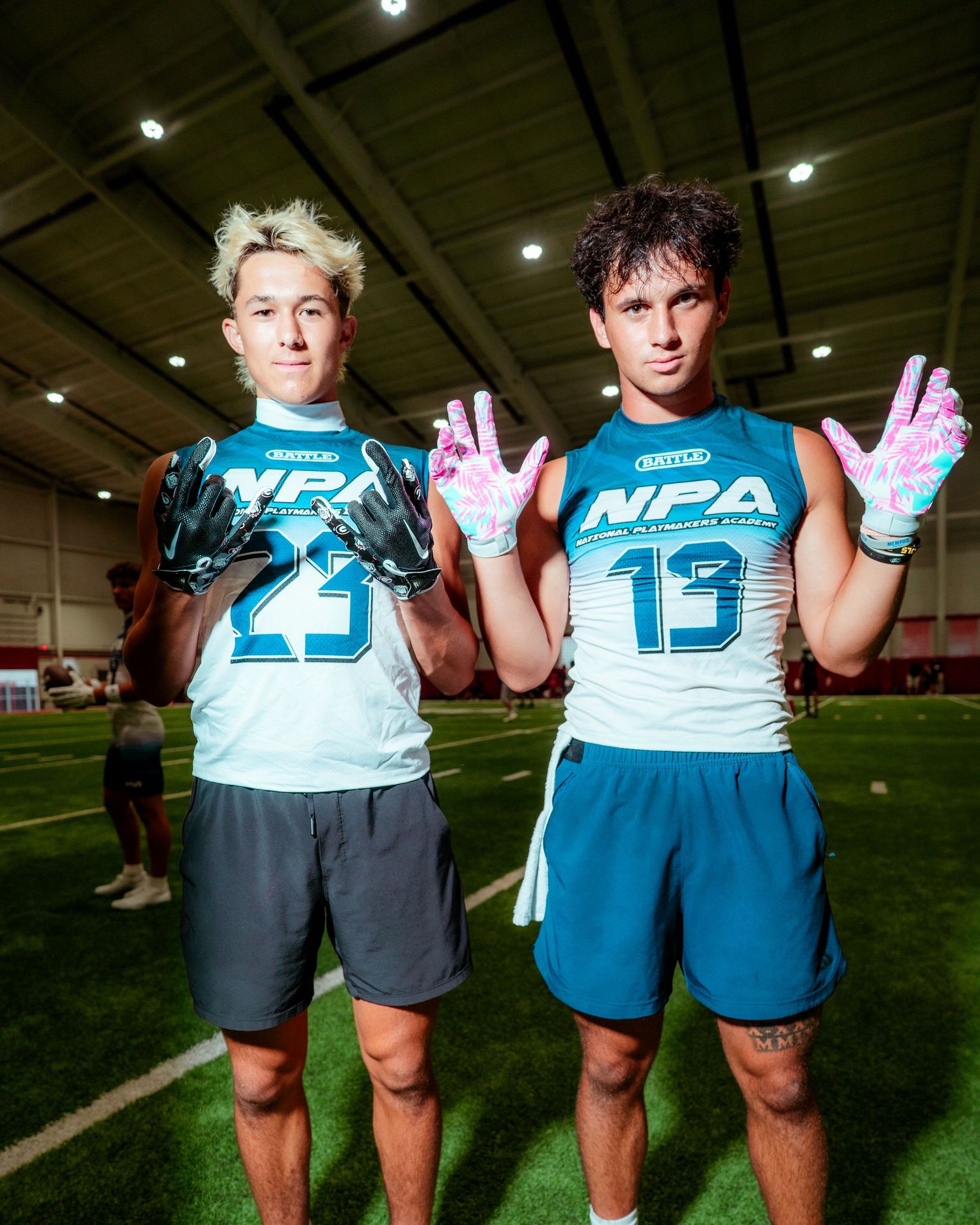 Two young football players in NPA jerseys numbered 23 and 13 pose indoors showing off colorful receiver gloves.