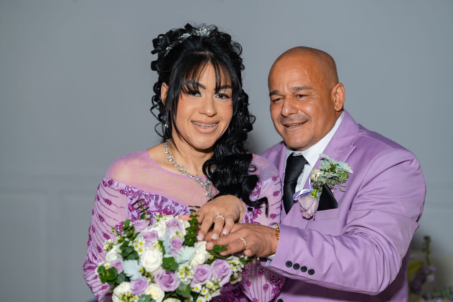 Bride and groom in lavender suit share a tender moment with a floral bouquet at their wedding.
