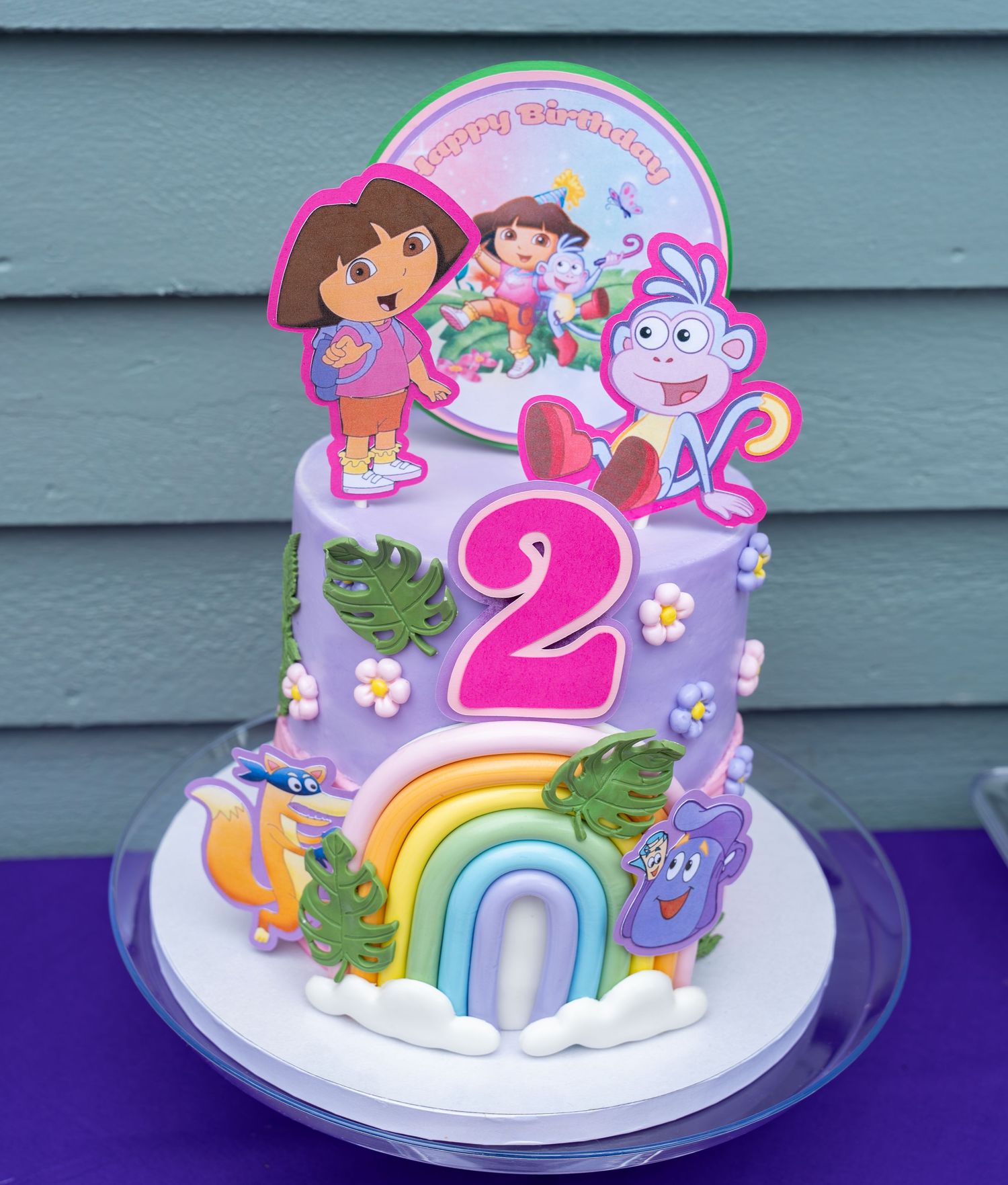 Two-tier purple Dora the Explorer themed birthday cake with rainbow decorations and number 2.