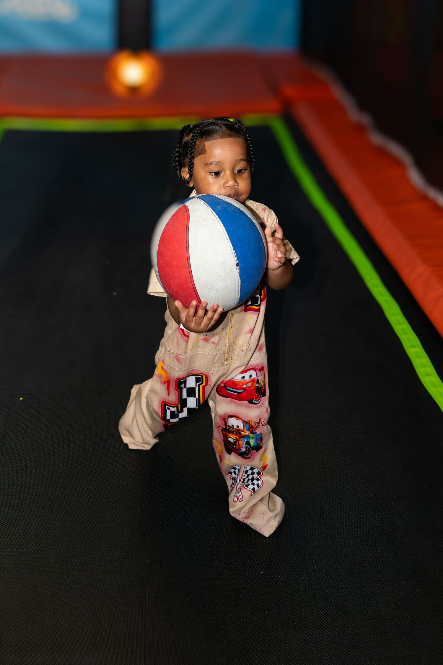 Young girl in Cars pajamas holding a colorful beach ball at an indoor trampoline park.