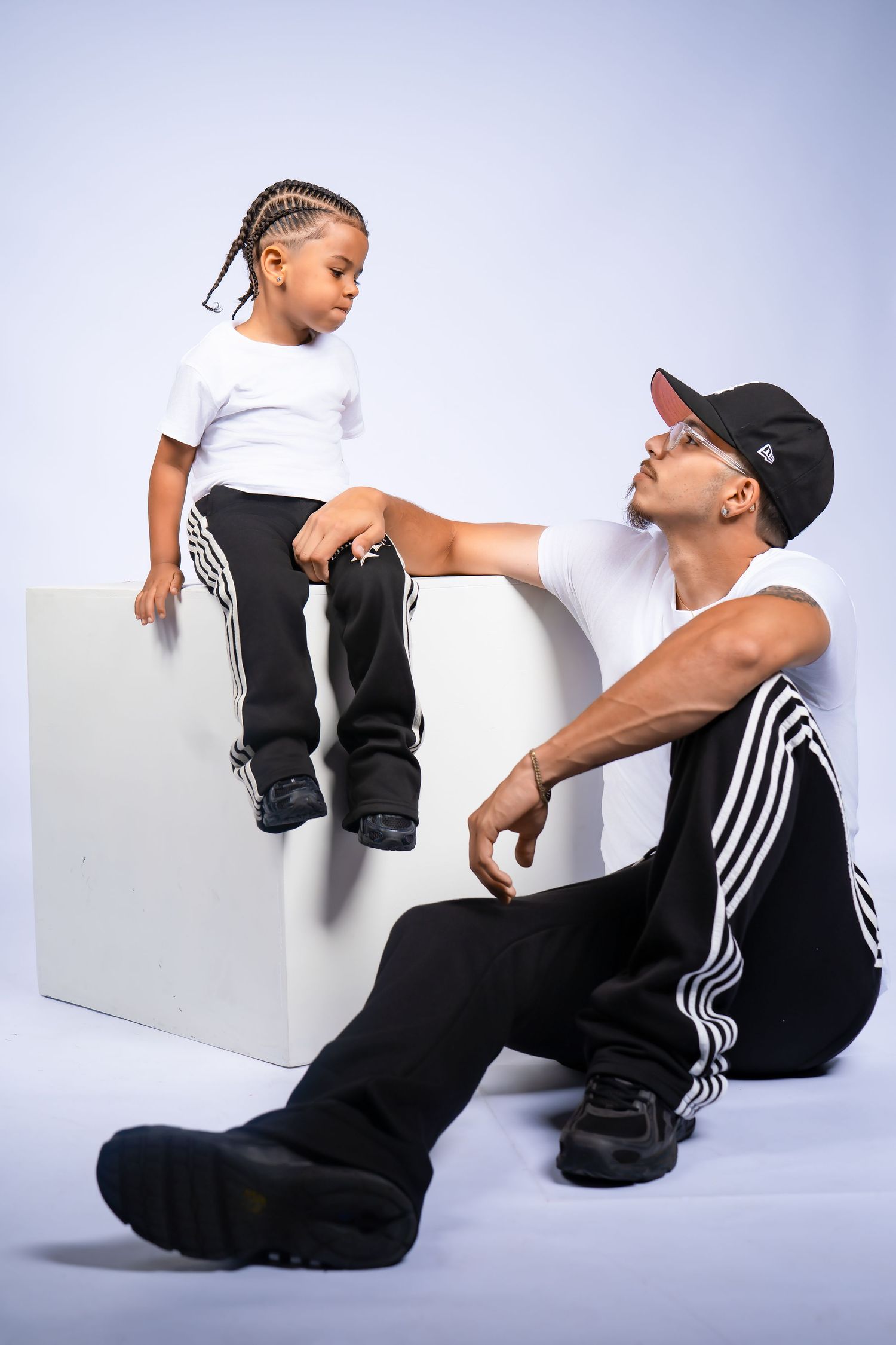 Father and son in matching white shirts and black Adidas pants posing in a professional studio.