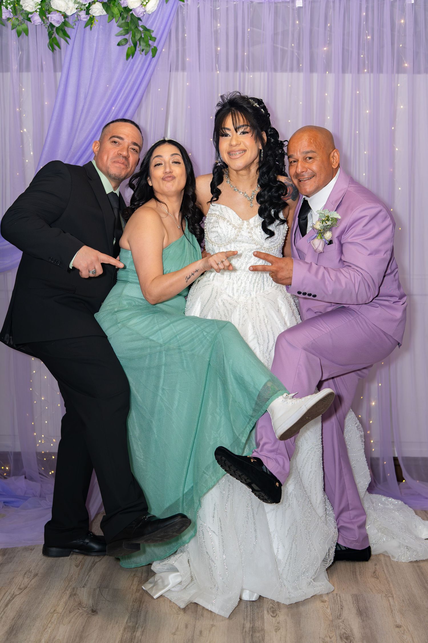 Four people pose joyfully at a wedding reception, bride in white gown with guests in formal attire.
